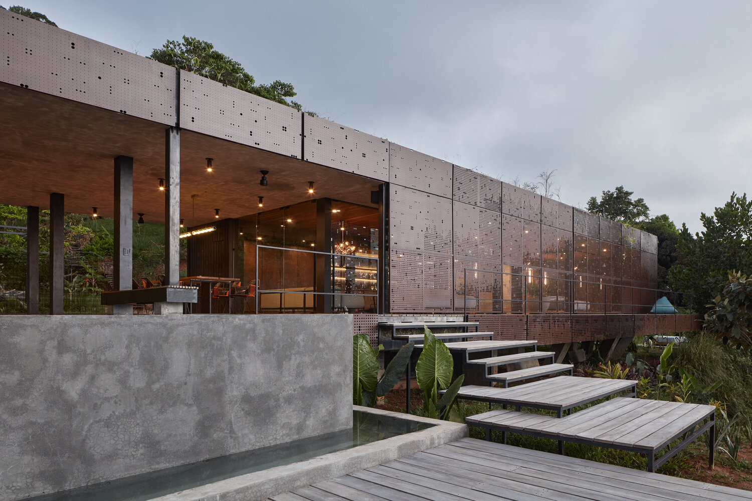 An infinity pool stretches along a partially covered patio, framing jungle and ocean views while offering shade from the tropical sun.