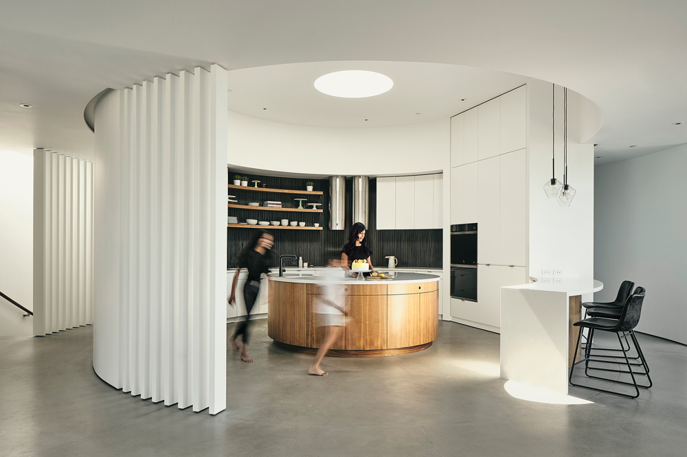 The former open courtyard becomes a circular kitchen, illuminated by a skylight that tracks daylight across custom curved cabinetry.