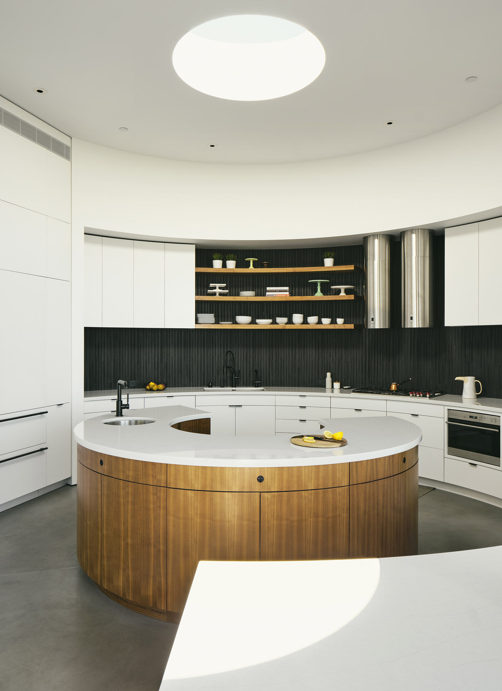 The former open courtyard becomes a circular kitchen, illuminated by a skylight that tracks daylight across custom curved cabinetry.