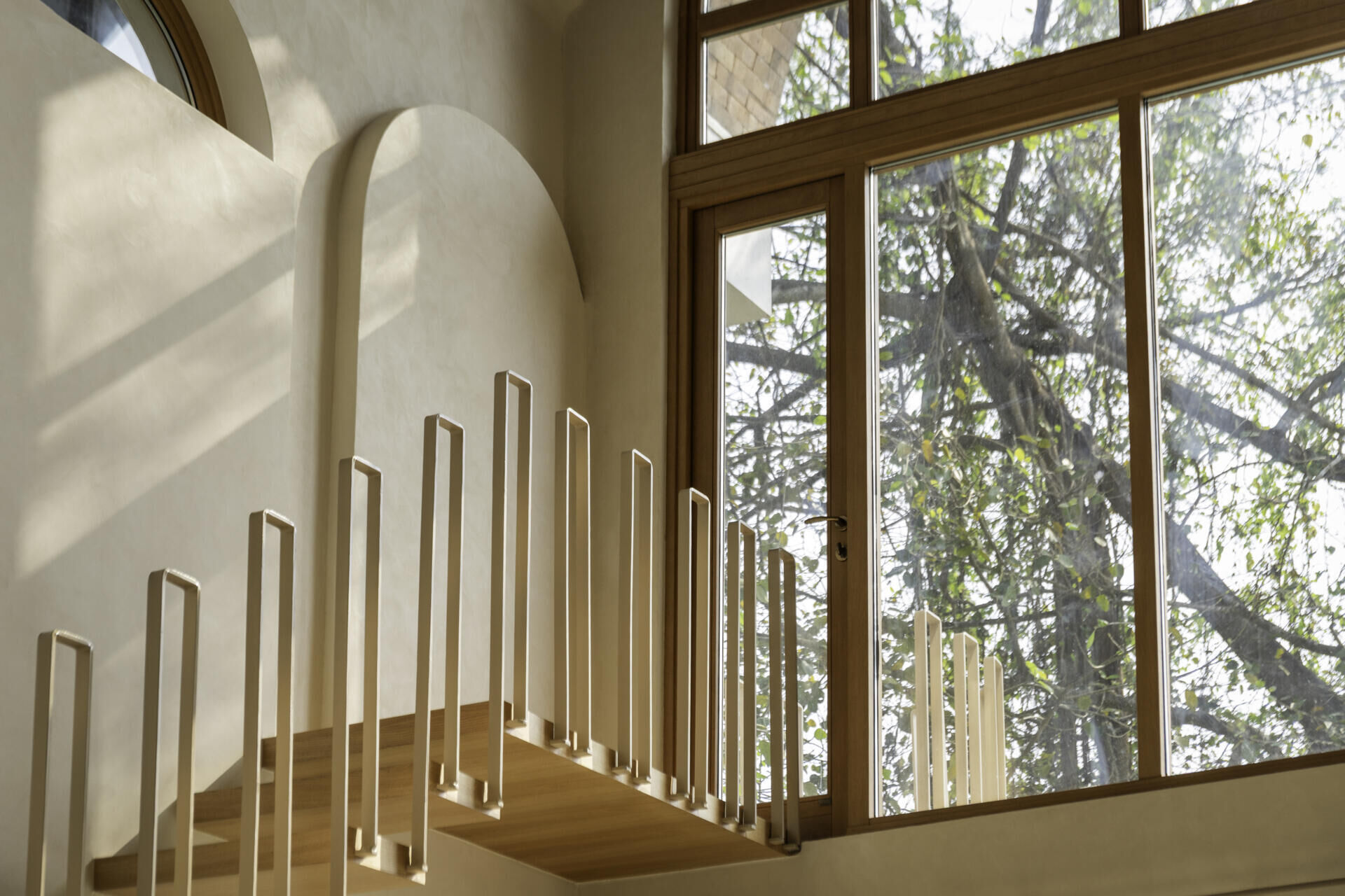 A compact staircase rises to a tiny balcony designed for one, creating a quiet vertical pause within the vaulted living area.