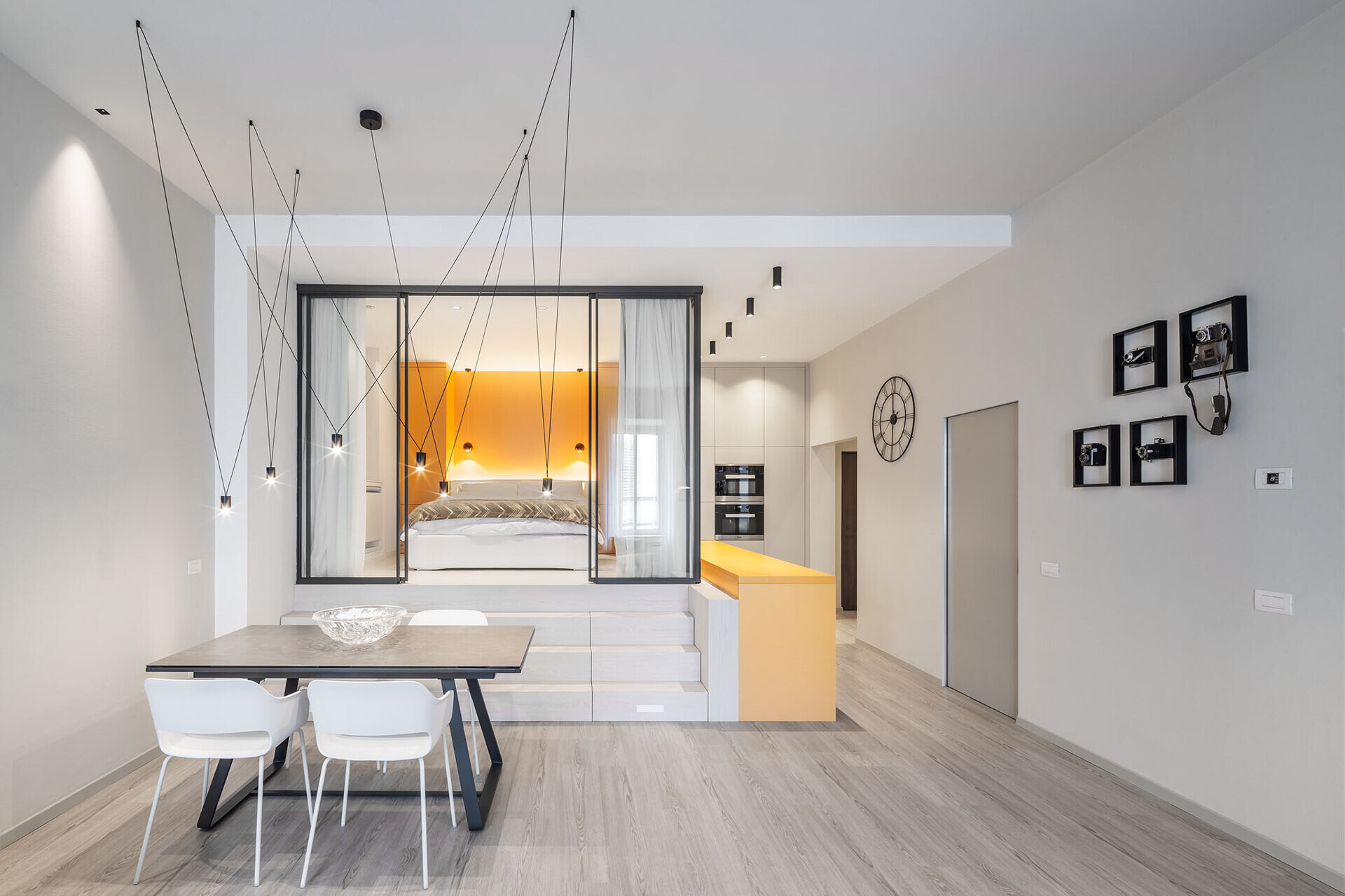 A glass enclosed bedroom sits on a mezzanine level, using ceiling height to separate spaces without closing them off.