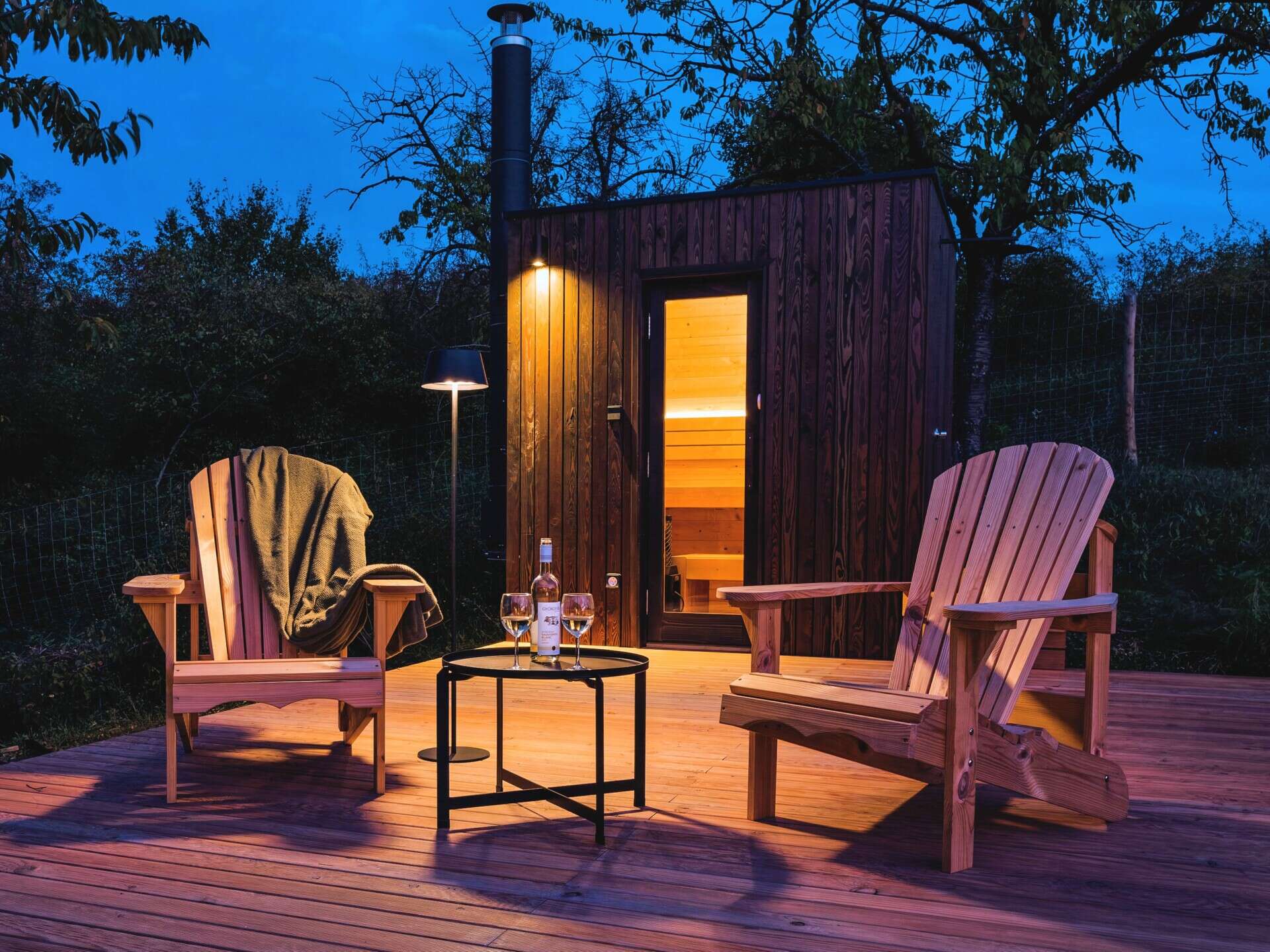As night falls, the cabin glows softly above the village below. The illuminated trapezoidal window turns this small structure into a quiet landmark in the Hungarian hills, showing how thoughtful design transforms even the simplest form.