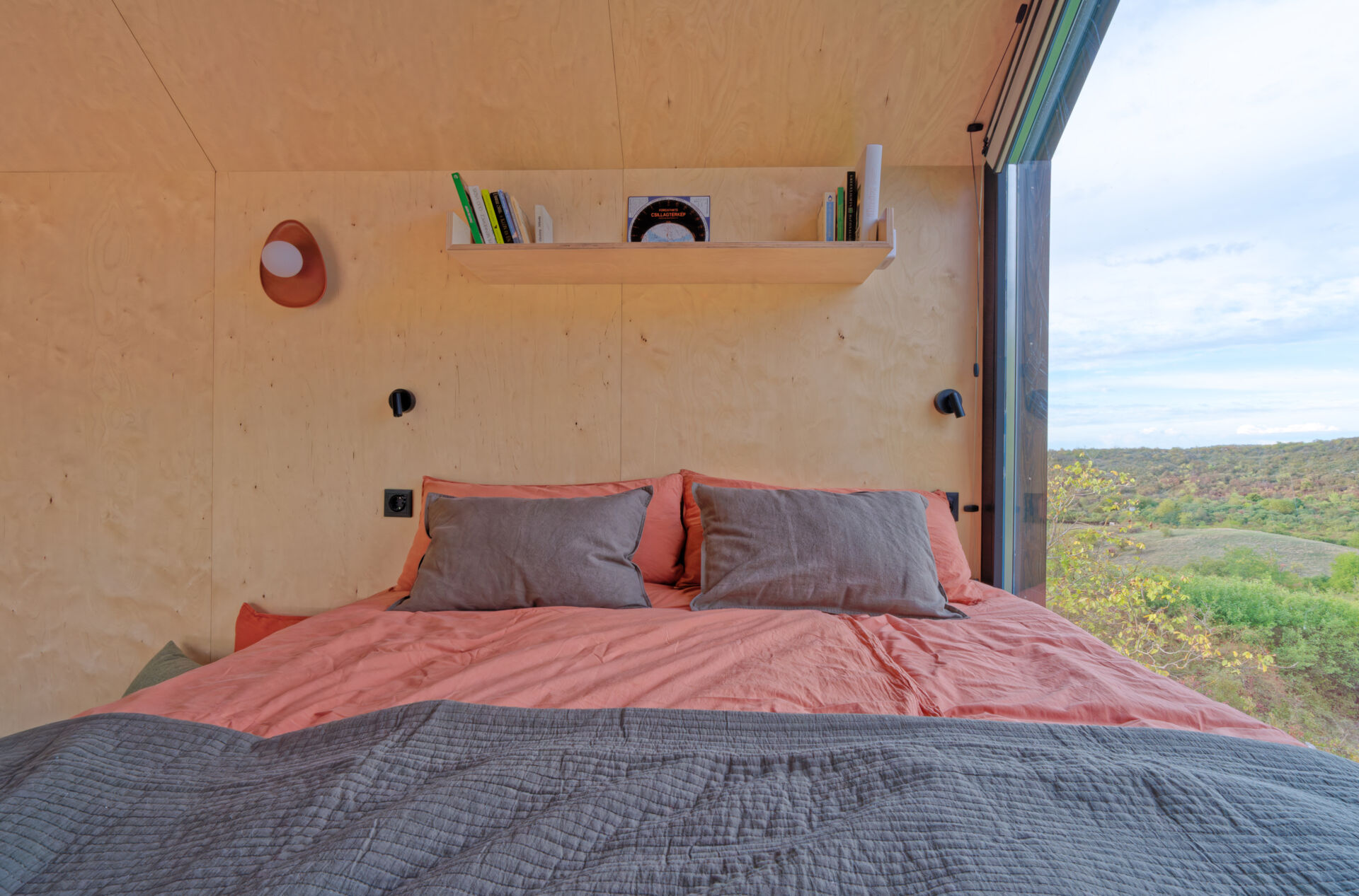 Light birch plywood, a visible gabled roof, and a striking trapezoidal window make this micro cabin interior feel surprisingly spacious. Included in the cabin is a sleeping area, lounge, kitchen, loft, and bathroom.