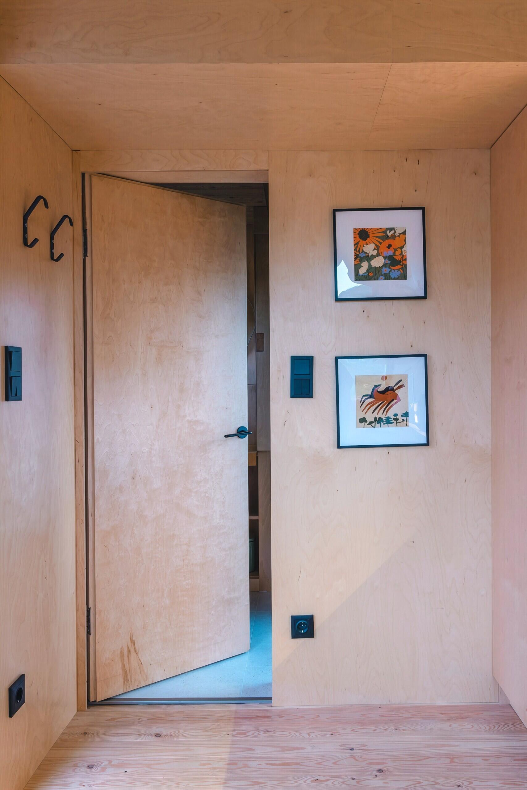 Light birch plywood, a visible gabled roof, and a striking trapezoidal window make this micro cabin interior feel surprisingly spacious. Included in the cabin is a sleeping area, lounge, kitchen, loft, and bathroom.