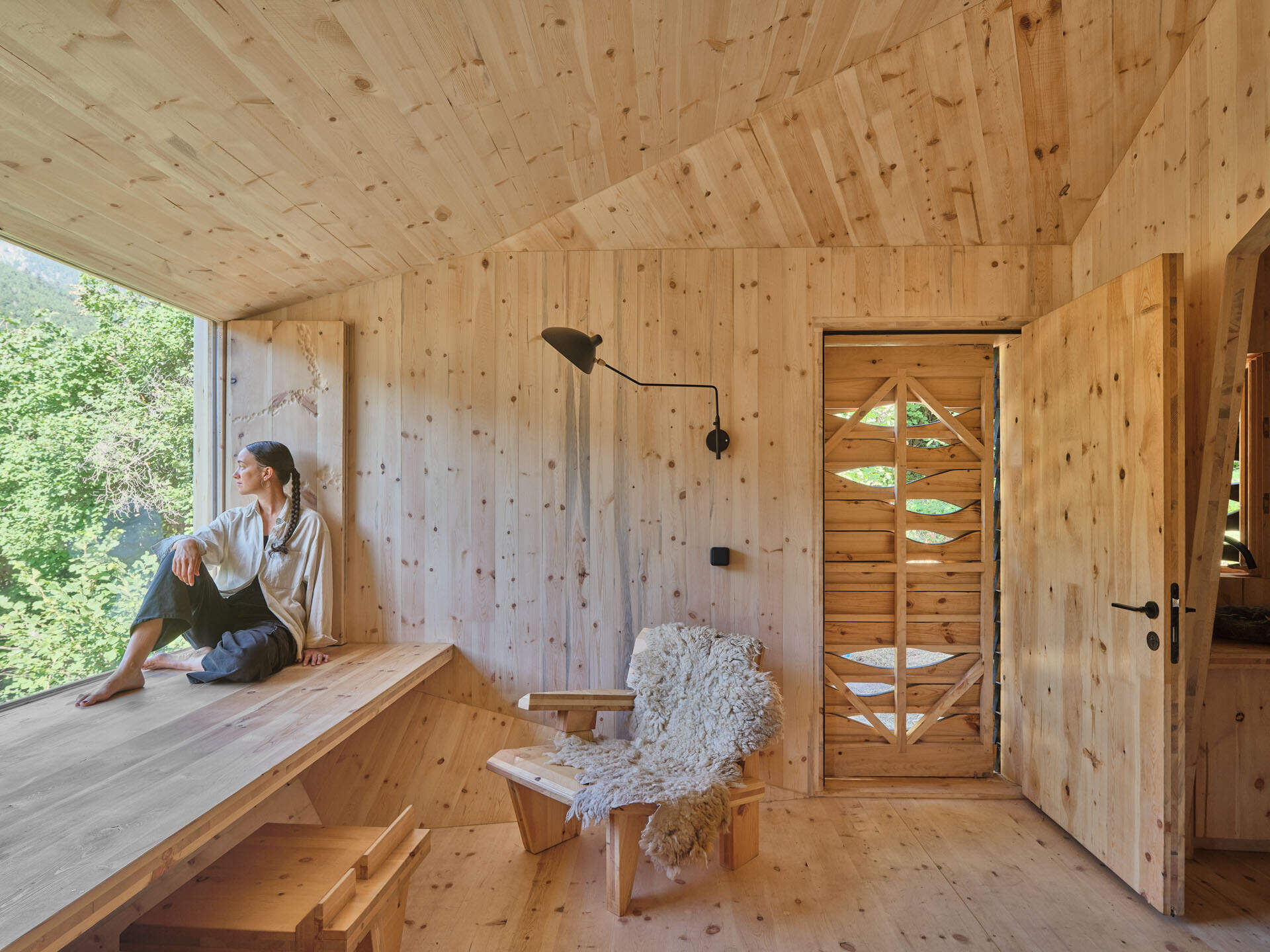 Inside a small cabin, custom timber furniture, a carved stone basin, and wool textiles connect local craftsmanship with design.