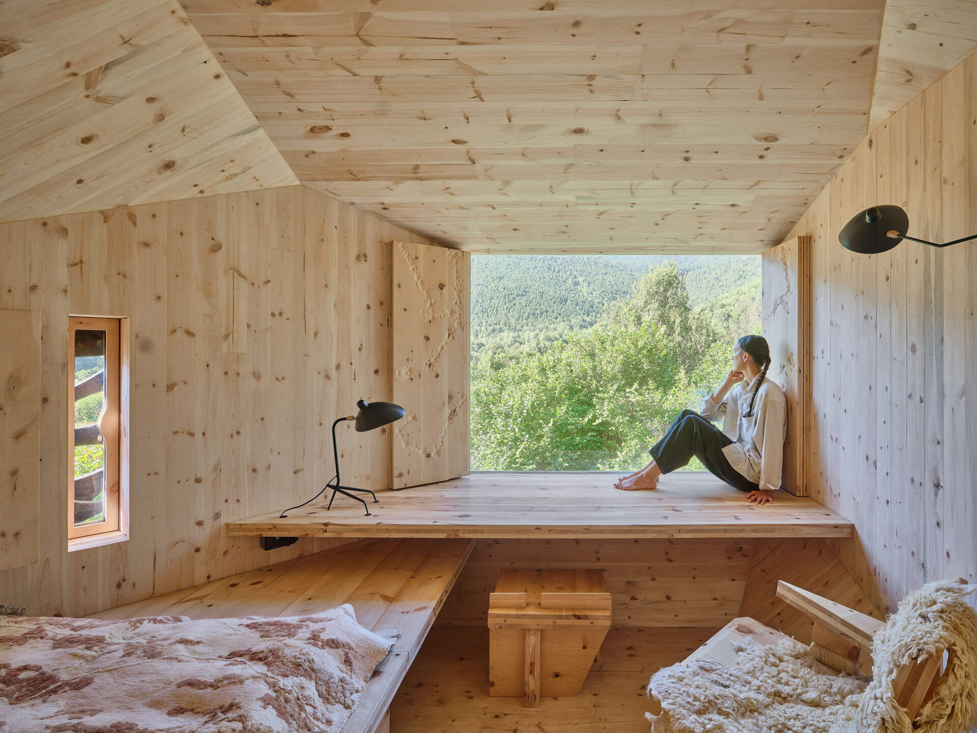 Inside a small cabin, custom timber furniture, a carved stone basin, and wool textiles connect local craftsmanship with design.