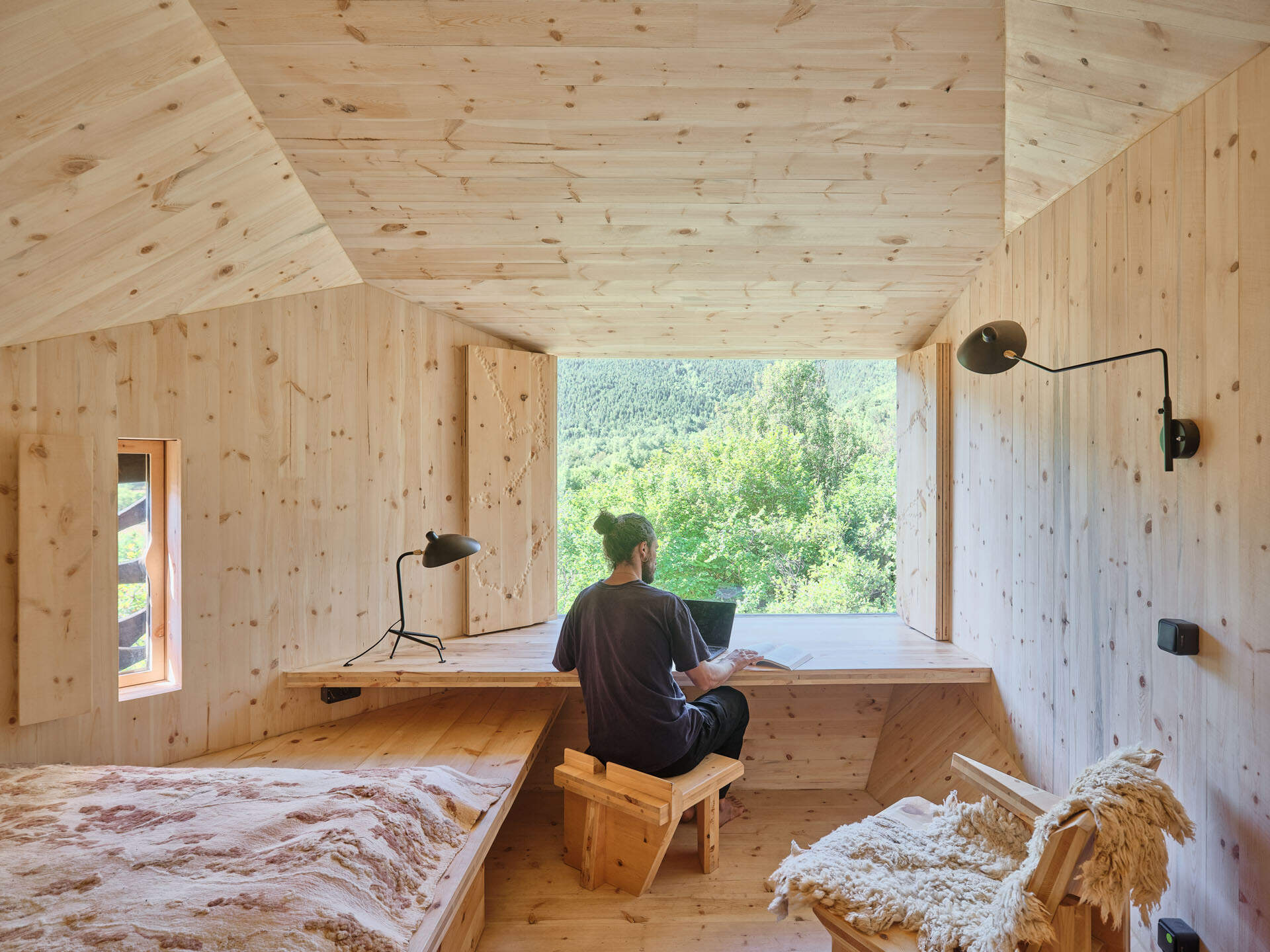 Inside a small cabin, custom timber furniture, a carved stone basin, and wool textiles connect local craftsmanship with design.