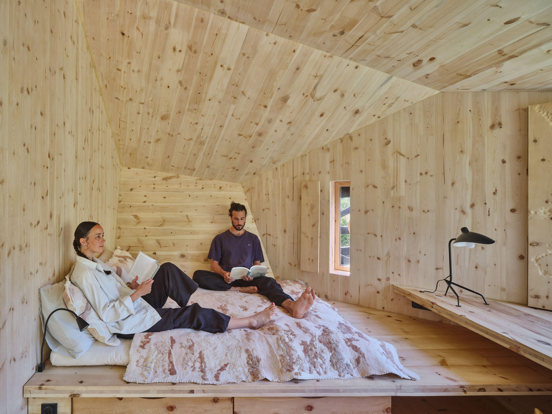 Inside a small cabin, custom timber furniture, a carved stone basin, and wool textiles connect local craftsmanship with design.