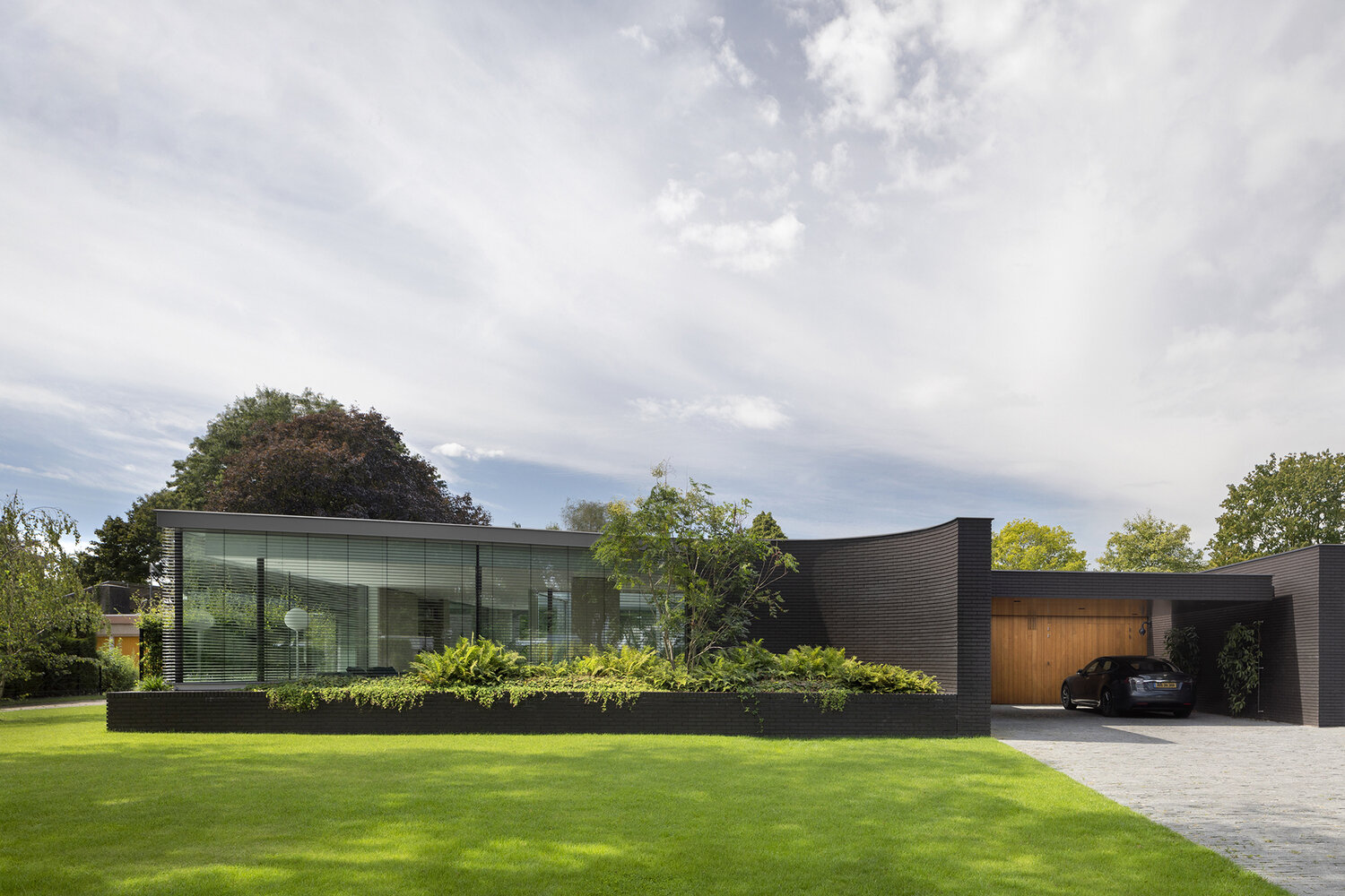 Las paredes curvas de ladrillo negro y las jardineras empotradas llenas de vegetación aportan una sensación audaz y natural a esta moderna villa holandesa.