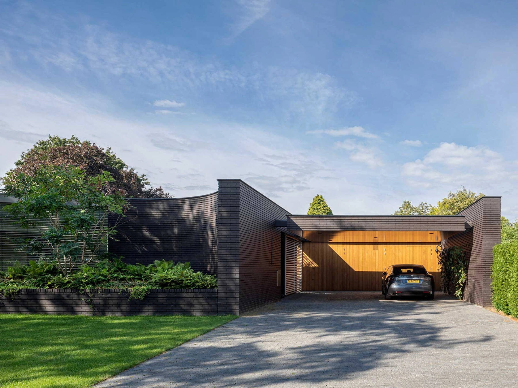 Las paredes curvas de ladrillo negro y las jardineras empotradas llenas de vegetación aportan una sensación audaz y natural a esta moderna villa holandesa.