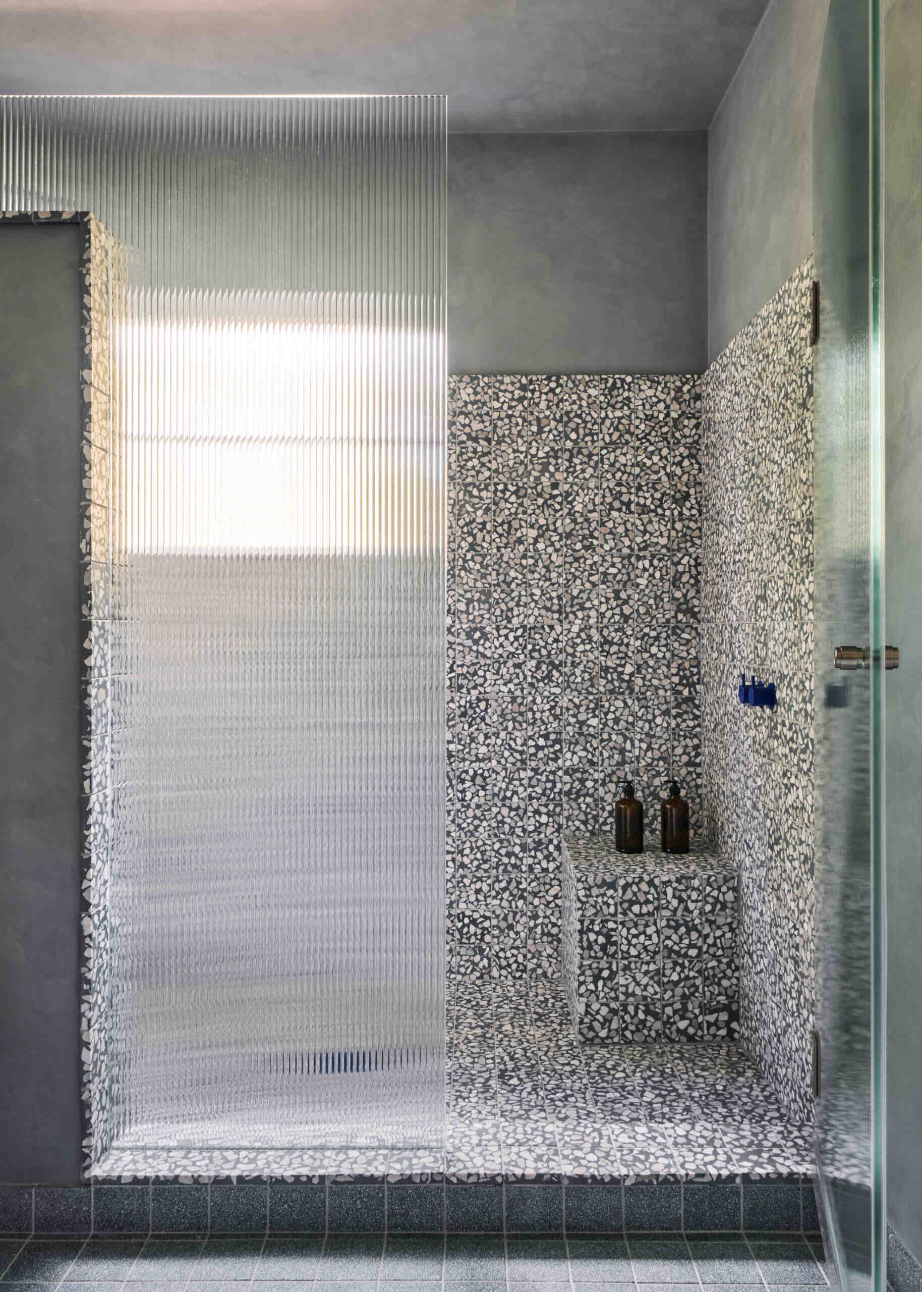 In this bathroom, speckled terrazzo that adds texture to the shower without overwhelming the space, while ribbed glass filters the light, diffusing it gently across the surfaces.