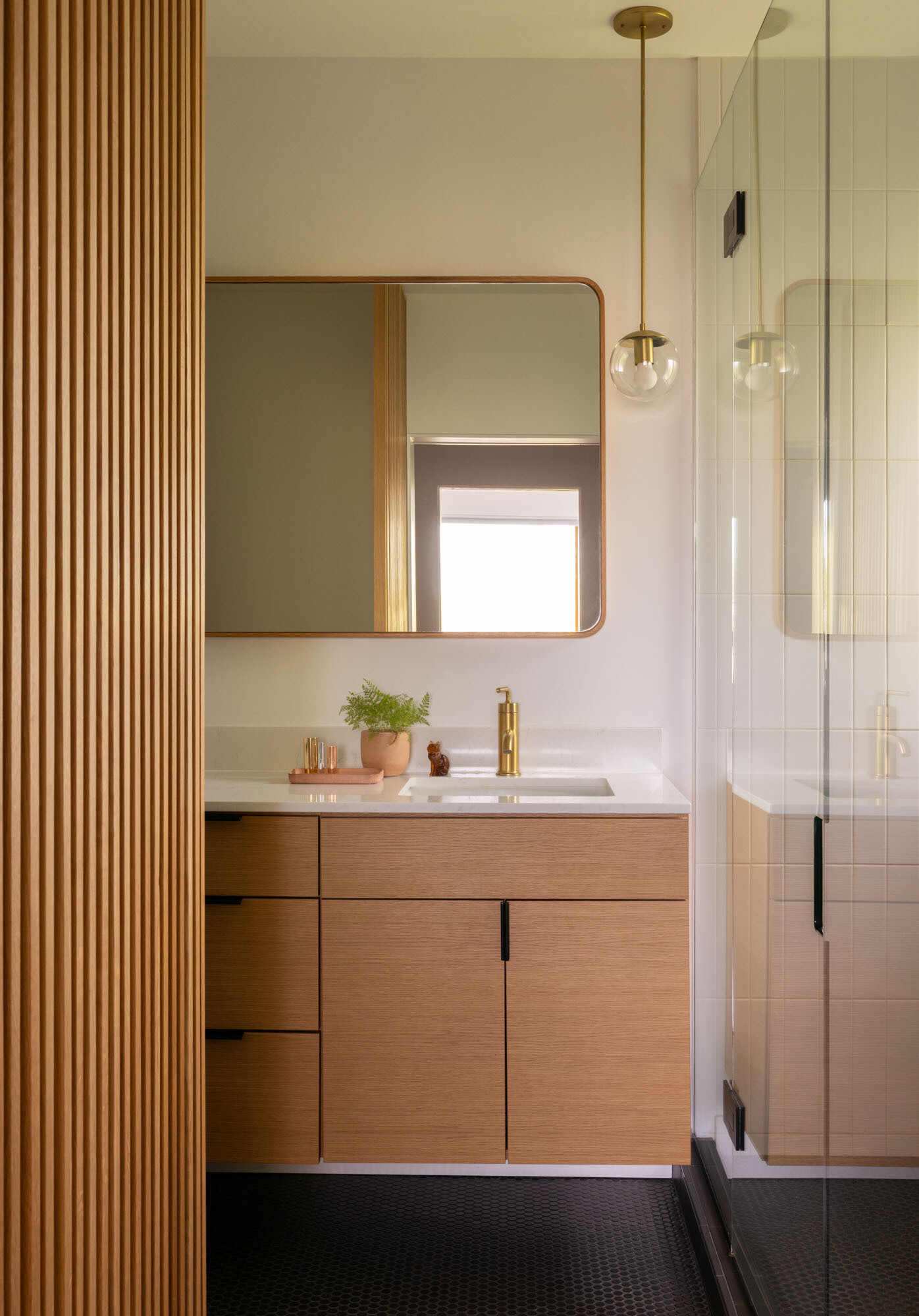 White subway tiles, graphite penny flooring, and warm wood accents create a bathroom that feels clean, modern, and inviting.