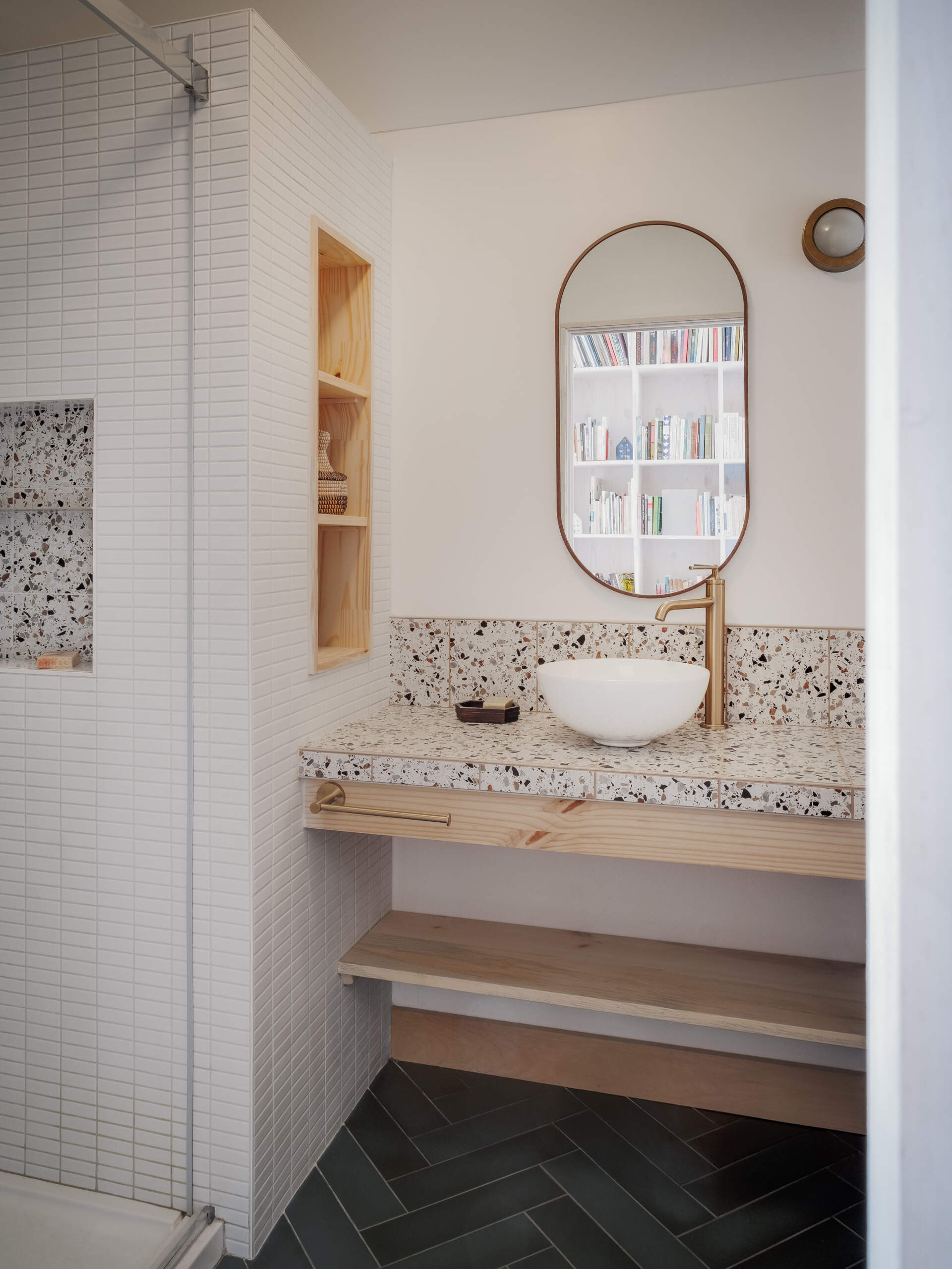 El moderno baño cuenta con un tocador de terrazo y madera con nichos de estantes incorporados.