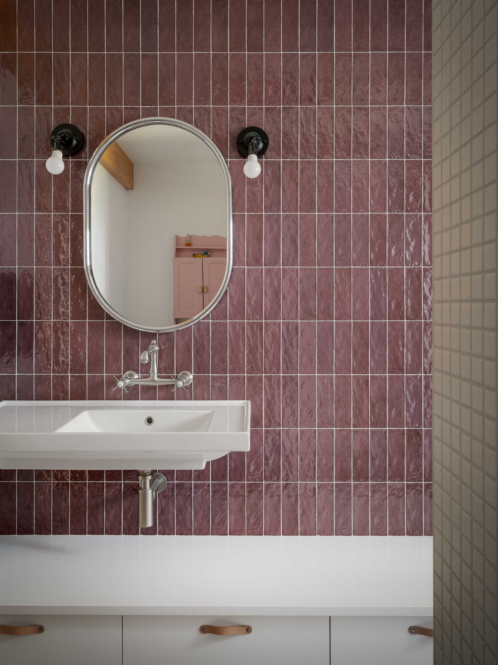 Los baños introducen un cambio de tono a través del color y la textura. Elegantes azulejos de color rosa envuelven las paredes, capturando la luz y agregando profundidad, mientras que un lavabo montado en la pared mantiene el piso despejado y le da a la habitación una sensación un poco más abierta.