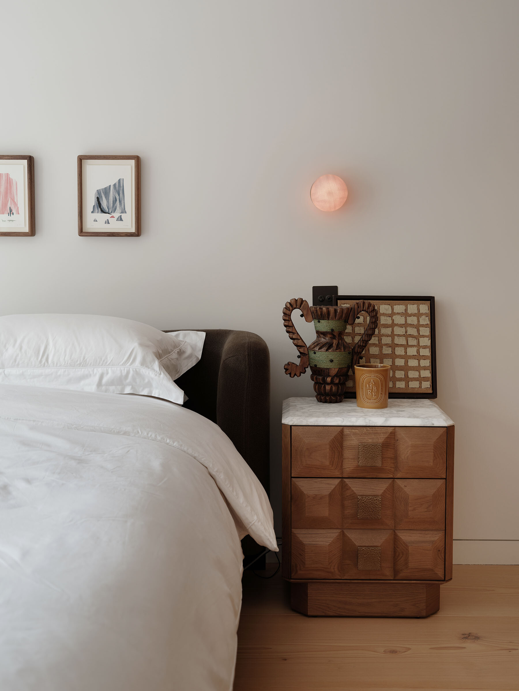 On the first floor, the primary bedroom has a simple palette of timber flooring, neutral walls, and carefully selected furniture, allowing small details to stand out. A marble-topped bedside table and warm-toned lighting introduce texture without overwhelming the space.