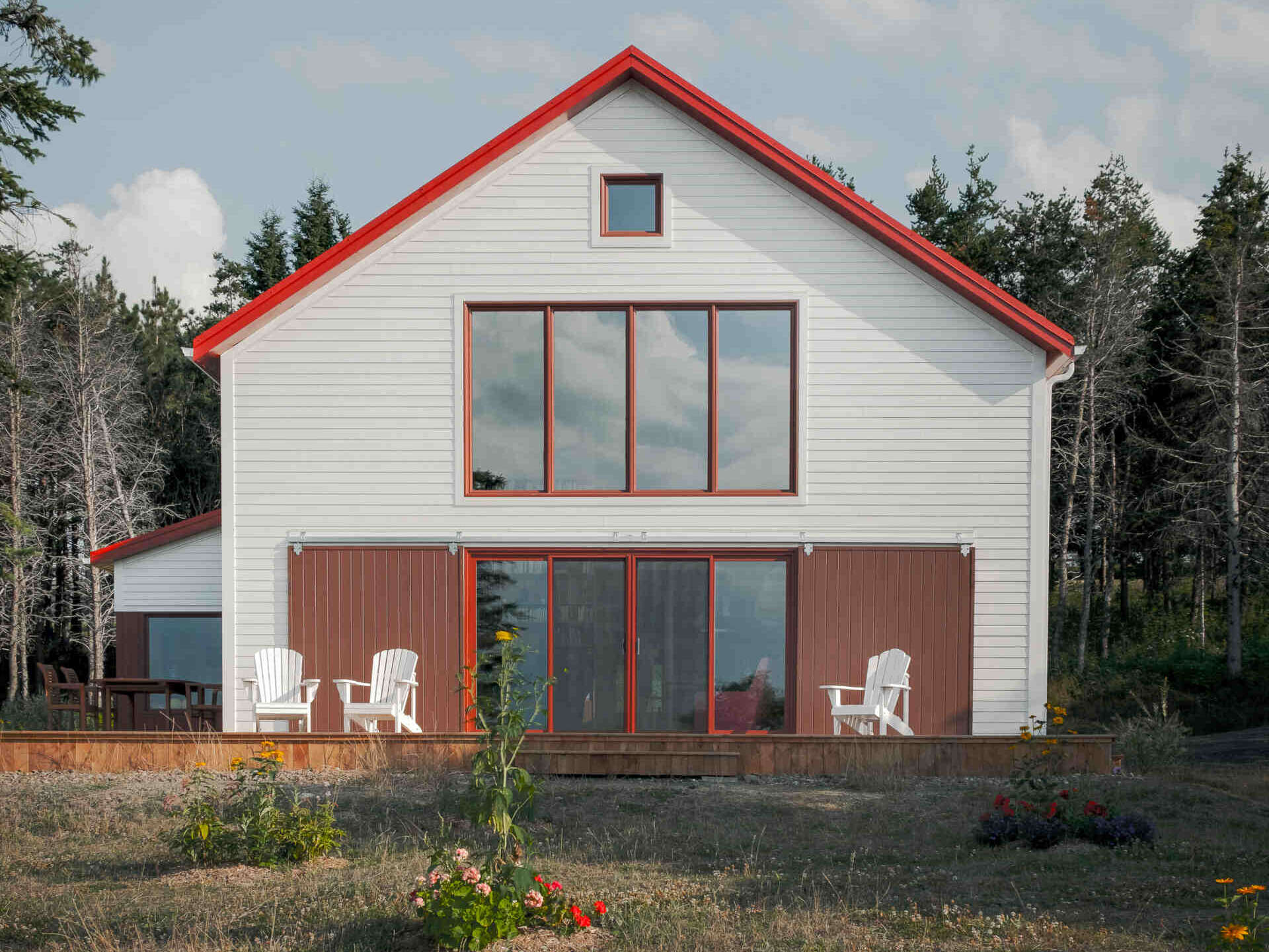 A modern home inspired by historic fishing sheds, has a simple shed form with wood, metal, and bold red shutters that create a striking yet familiar exterior.