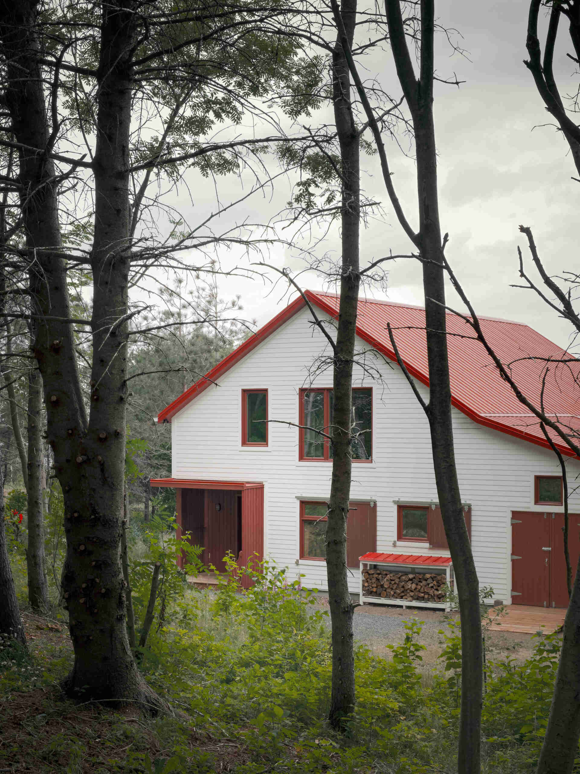 Inspirada en las históricas chozas de pesca, esta casa moderna toma la forma de un cobertizo simple, que utiliza madera, metal y atrevidas contraventanas rojas para crear una apariencia llamativa pero familiar.