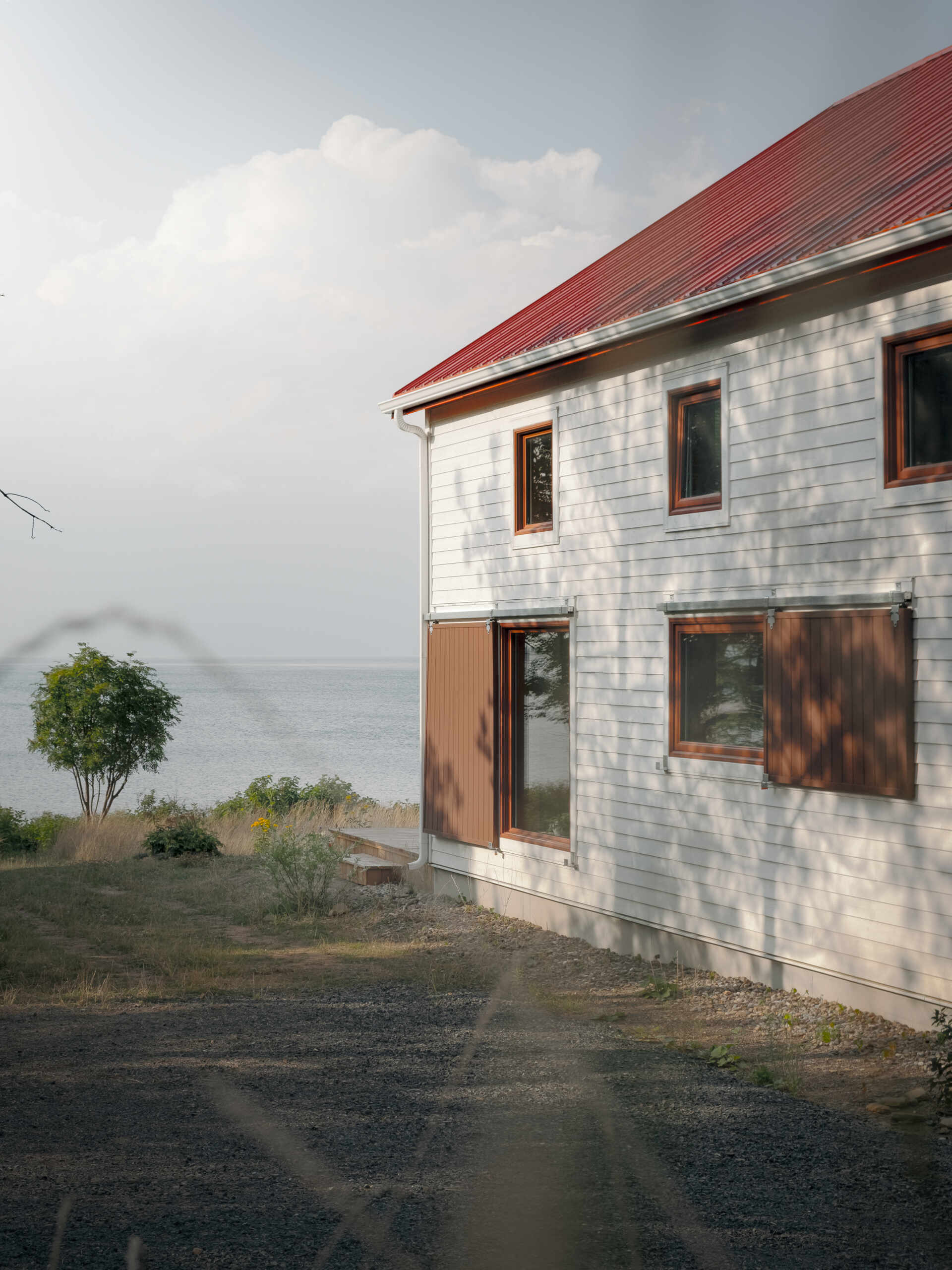 Inspirada en las históricas chozas de pesca, esta casa moderna toma la forma de un cobertizo simple, que utiliza madera, metal y atrevidas contraventanas rojas para crear una apariencia llamativa pero familiar.