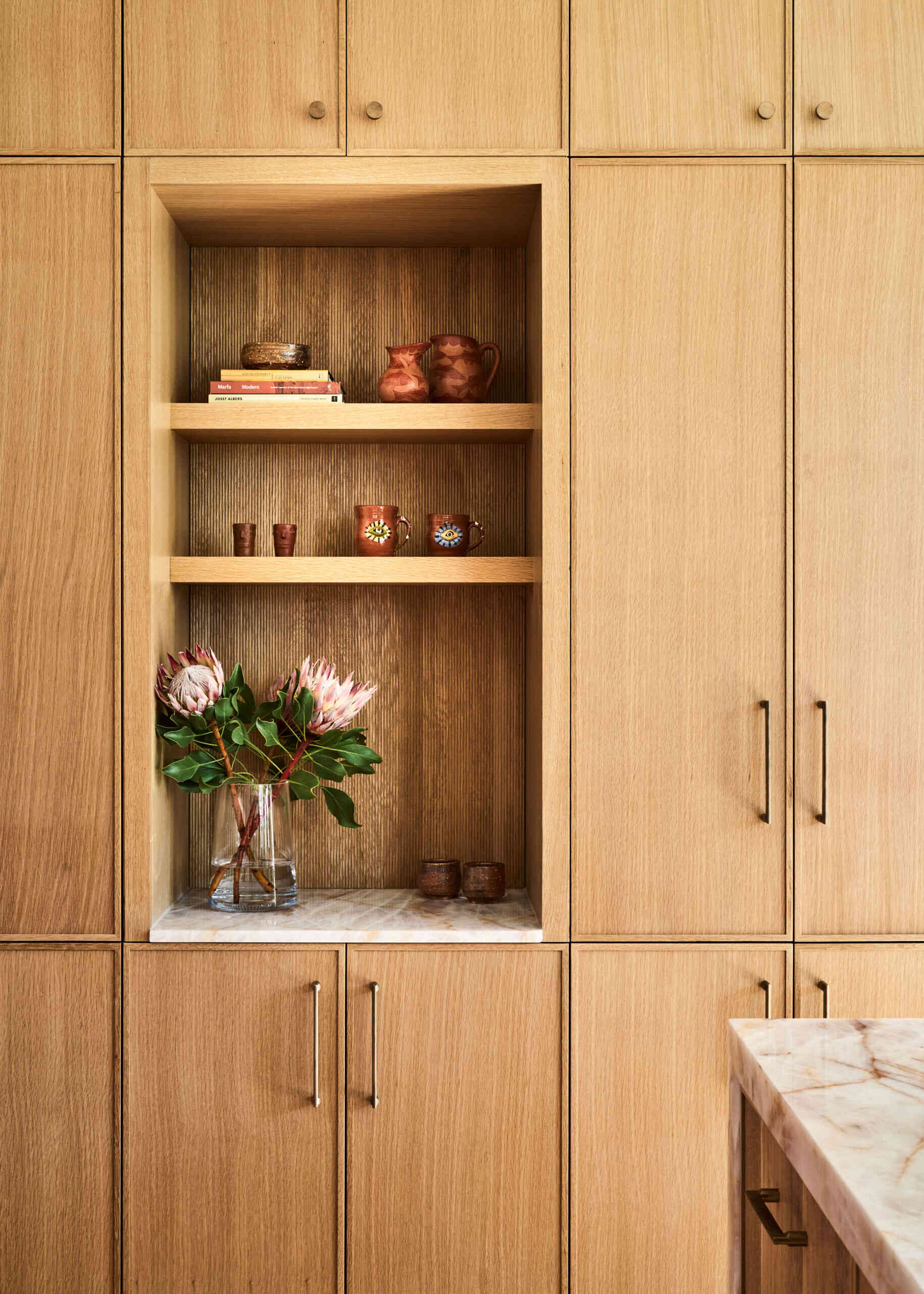 In the kitchen, wavy pink tiles, wood cabinets, rose quartz countertops, and a curved zellige hood create a playful yet refined space full of texture.