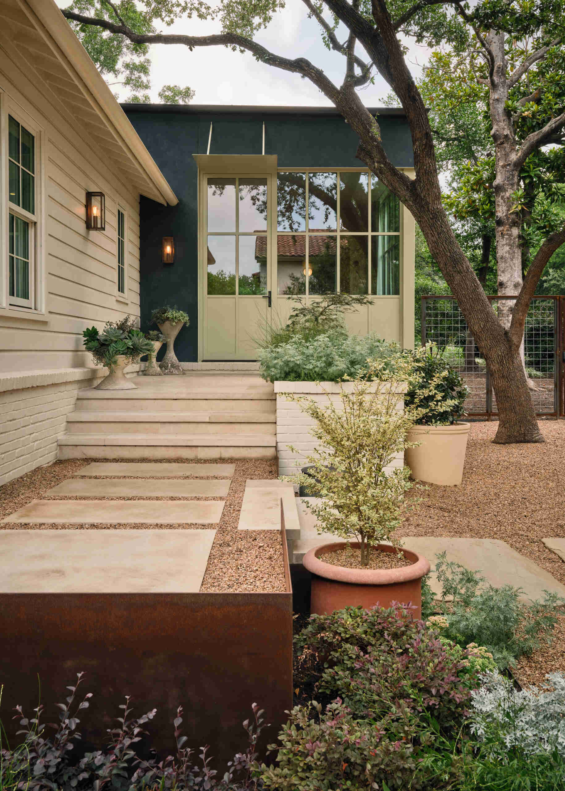 In the backyard, terraced planters and native landscaping create layered outdoor spaces leading to a terracotta-toned carport.