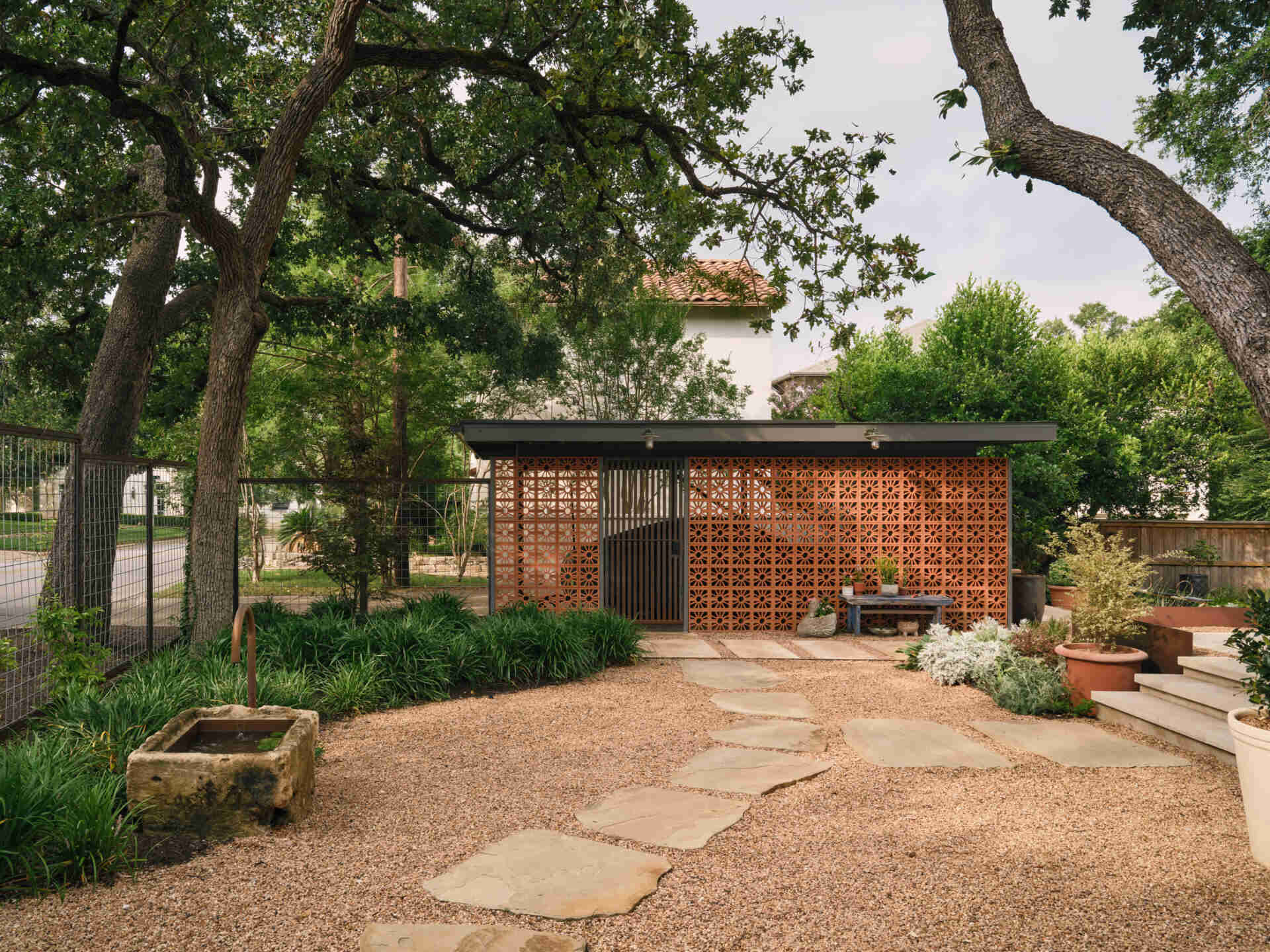 In the backyard, terraced planters and native landscaping create layered outdoor spaces leading to a terracotta-toned carport.