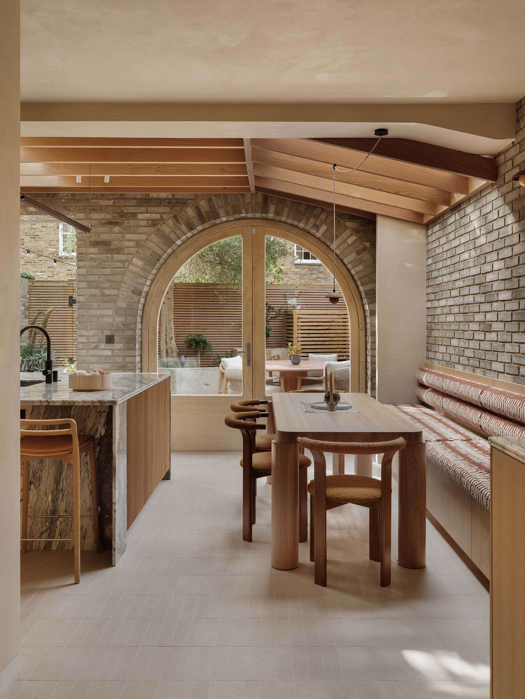 The dining area sits at the center of the open-plan arrangement. It connects directly to both the kitchen and living spaces, allowing it to function as part of a shared environment. The banquette offers seating along the wall, while skylights let natural light to fill the interior.