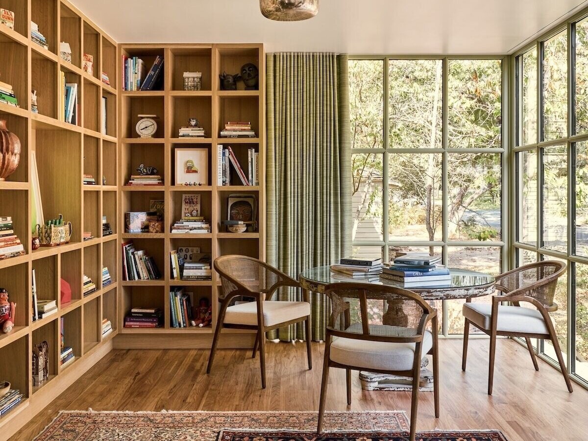 In the library, custom wood shelving and steel-framed windows create a calm, light-filled workspace connected to the garden.