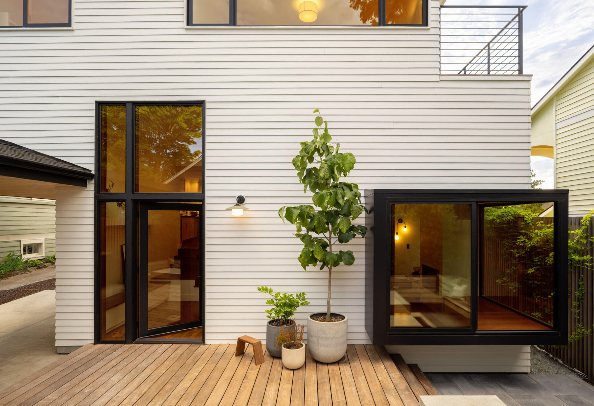 A compact backyard transforms into a layered outdoor retreat with a firepit, built-in seating, and a playful corner window connection.