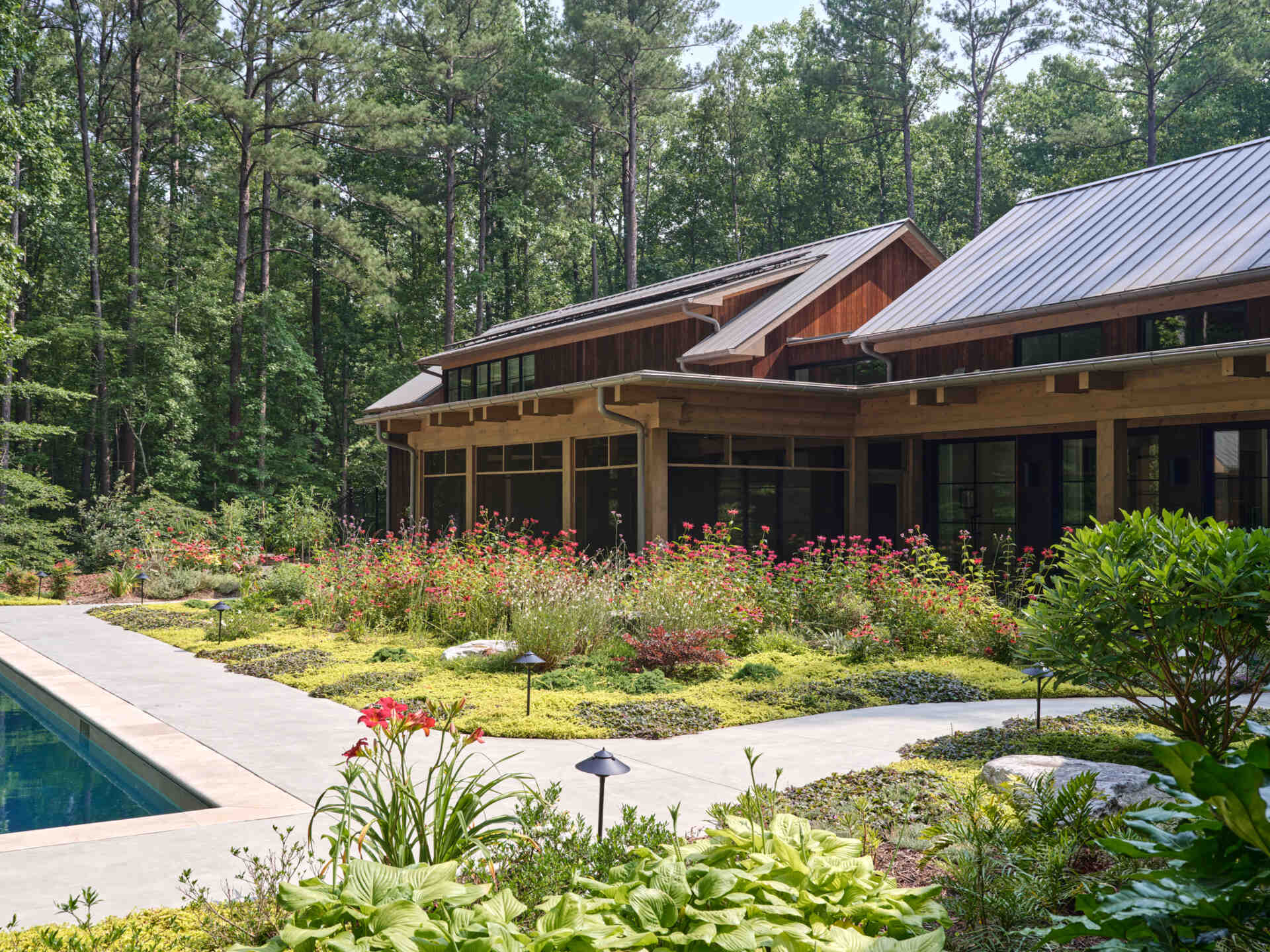 Double-height living, expansive windows, and a stone chimney define this warm, light-filled home in North Carolina, while an organized garden has room for a growing, relaxing, and enjoying the pool.