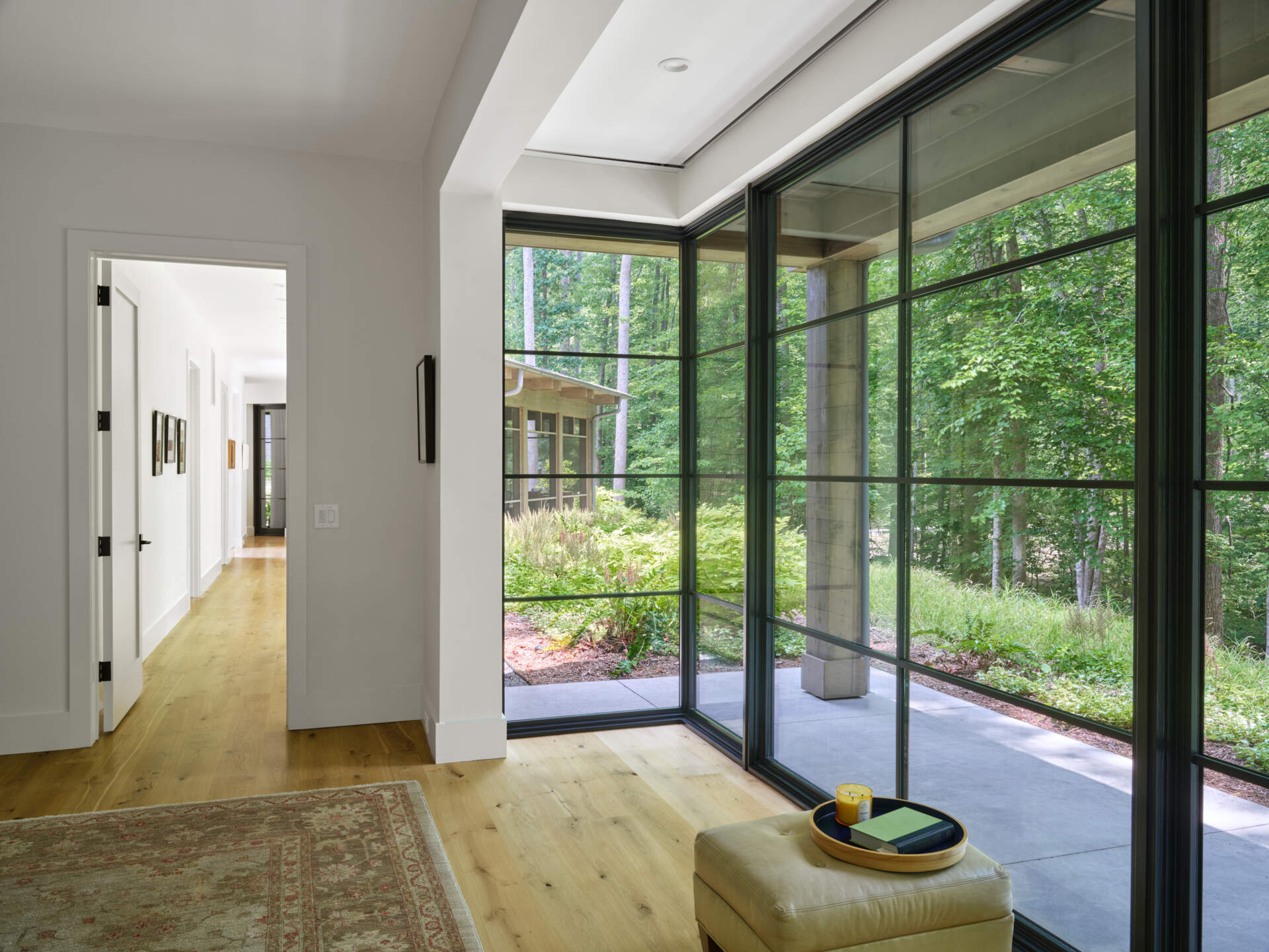 A window-lined hallway leads to the primary bedroom, pairing forest views with a gallery-style wall of art.