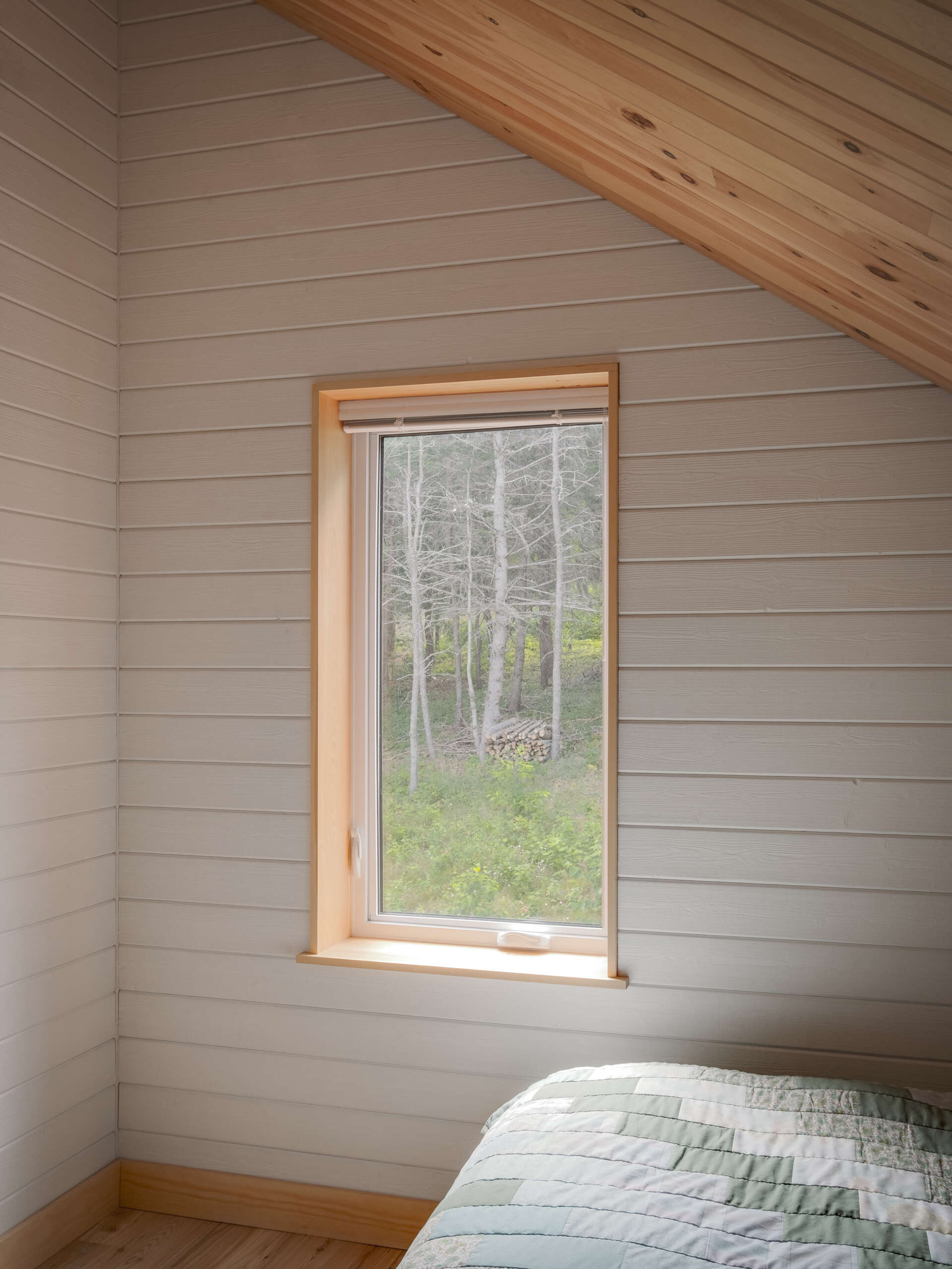 El moderno dormitorio cuenta con paredes de madera encaladas y ventanas con vistas a los árboles.