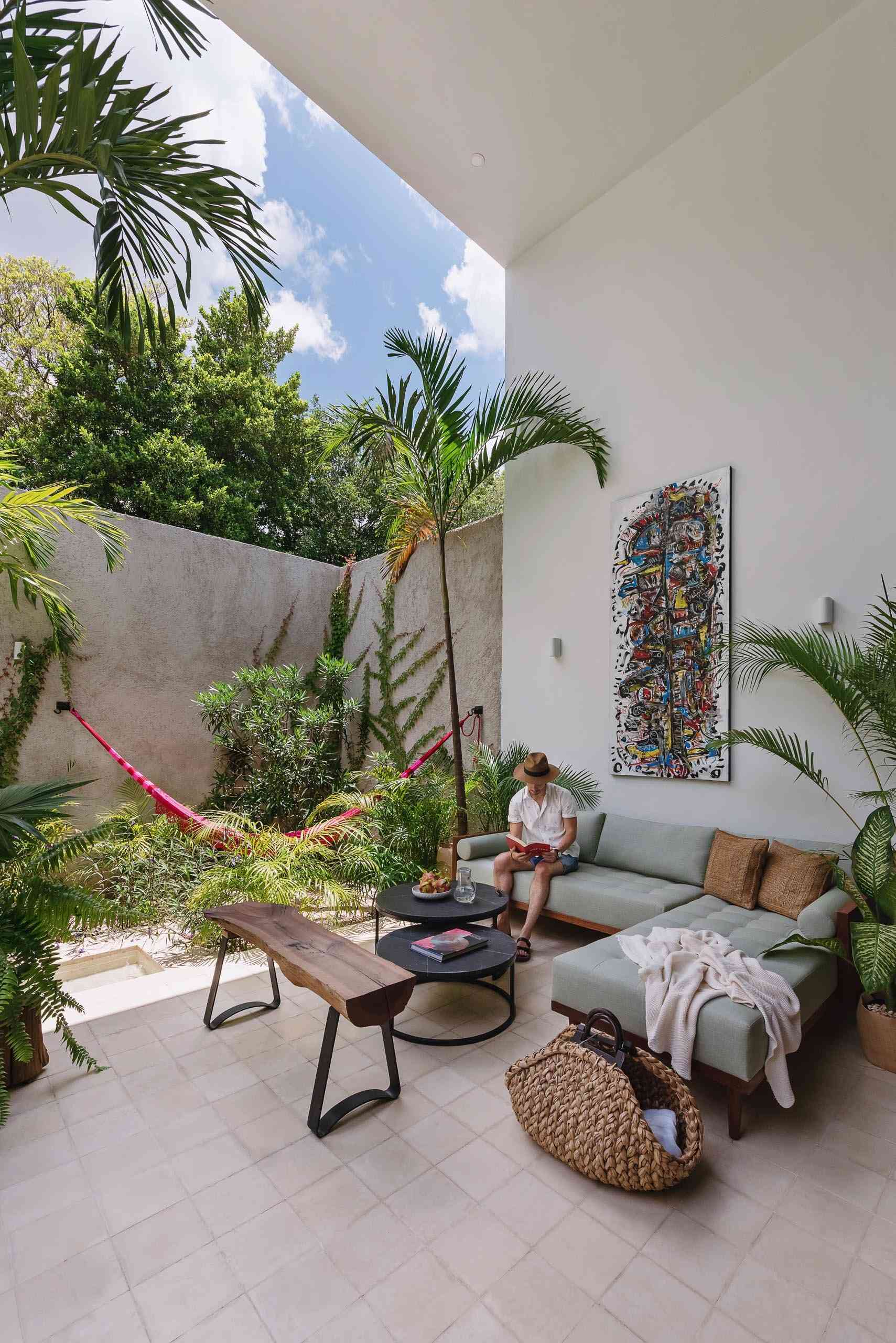 A small courtyard patio filled with tropical plants, colorful artwork, and relaxed seating creates a private outdoor living room inside this modern Mexican home.
