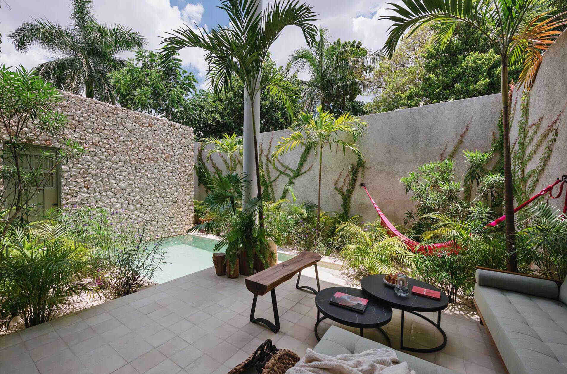 A small courtyard patio filled with tropical plants, colorful artwork, and relaxed seating creates a private outdoor living room inside this modern Mexican home.