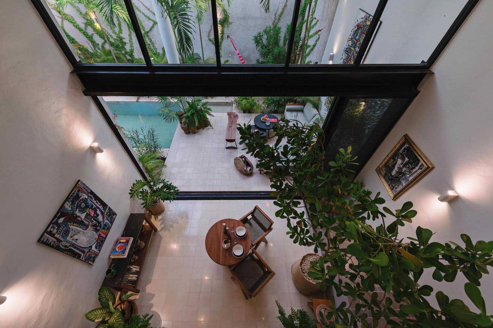 A small courtyard patio filled with tropical plants, colorful artwork, and relaxed seating creates a private outdoor living room inside this modern Mexican home.