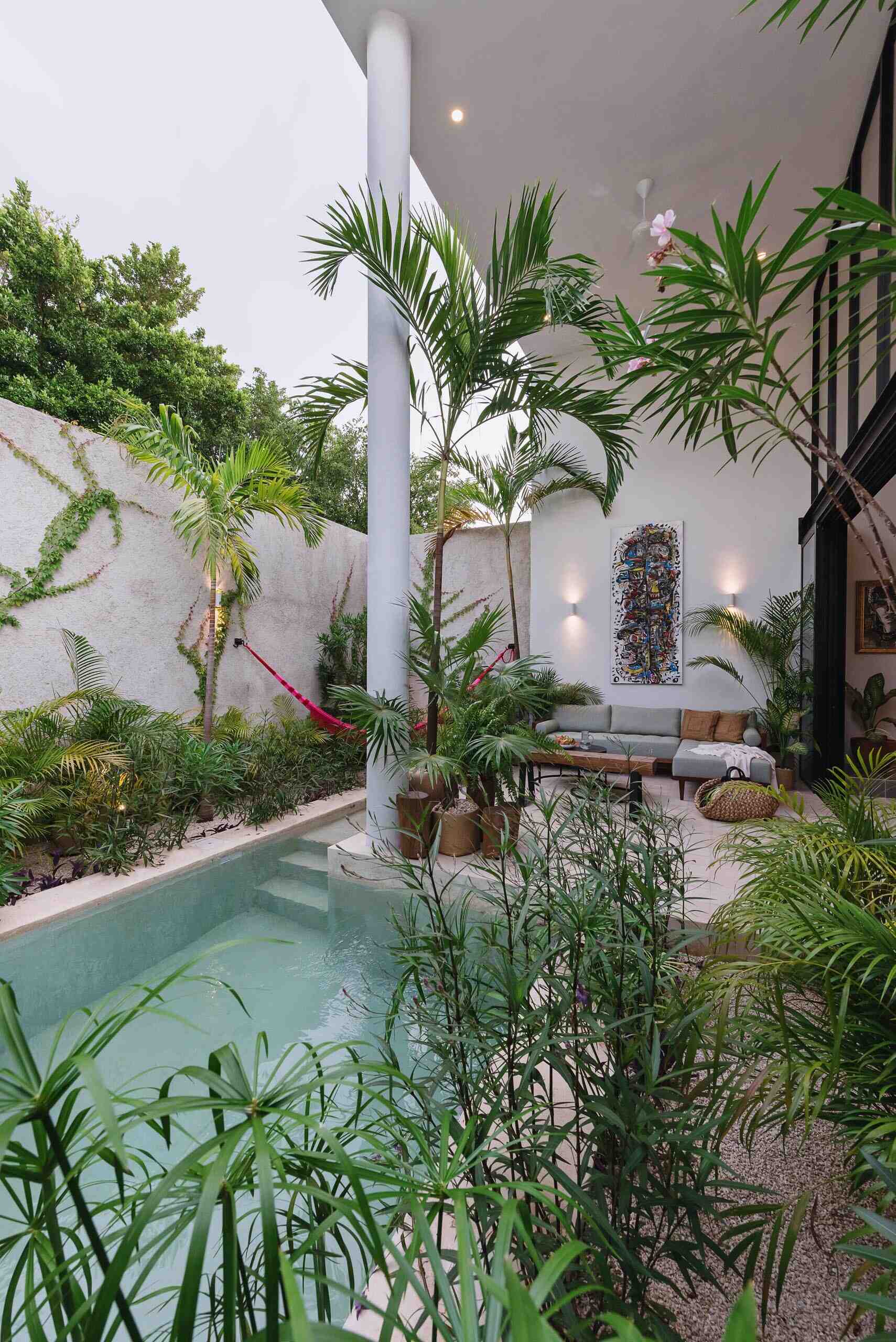A compact courtyard pool surrounded by tropical plants and a textured stone wall creates a peaceful place to cool off on warm days.