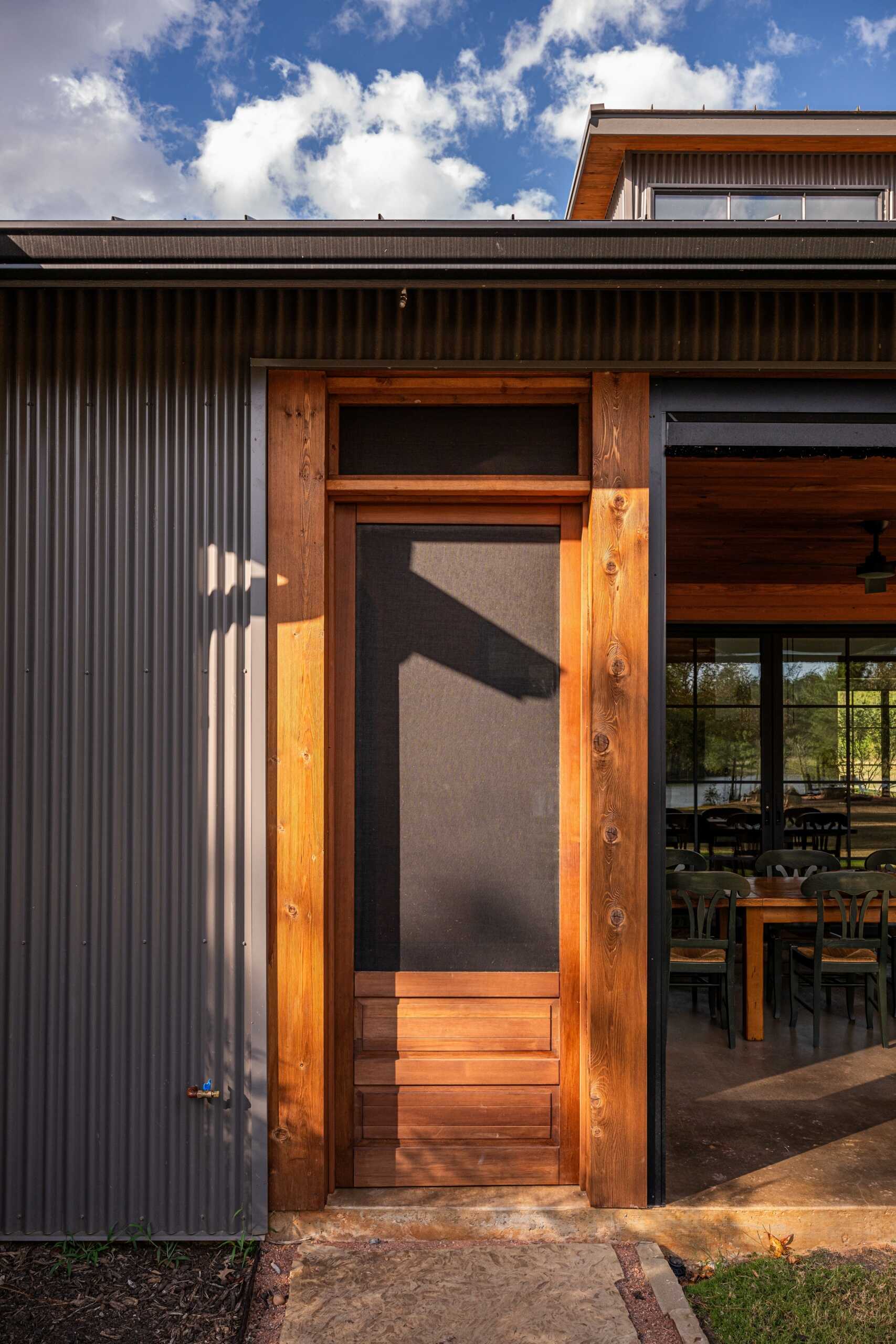 The patio extends the interiors. Fixed screen doors allow access when larger insect screens are deployed. The porch, furnished with a variety of seating area, is carefully proportioned to maximize light, ventilation, and visual connection to the pond and tree canopy, supporting both casual and formal gatherings.