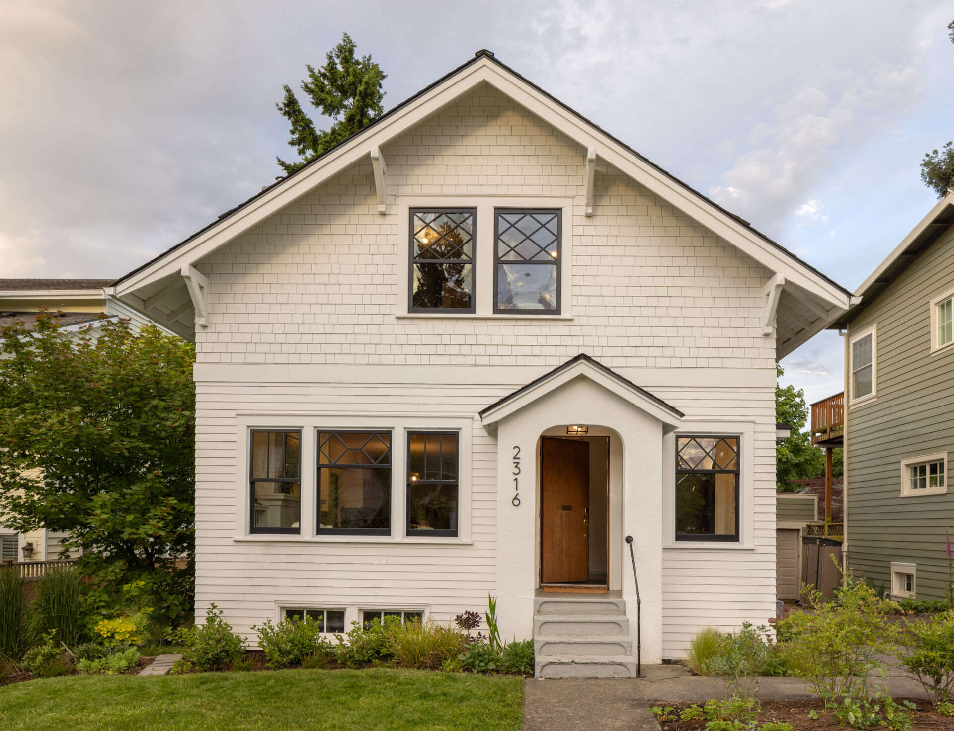 Classic white siding and black trim refresh this 1930s Craftsman facade while keeping its timeless street presence intact.