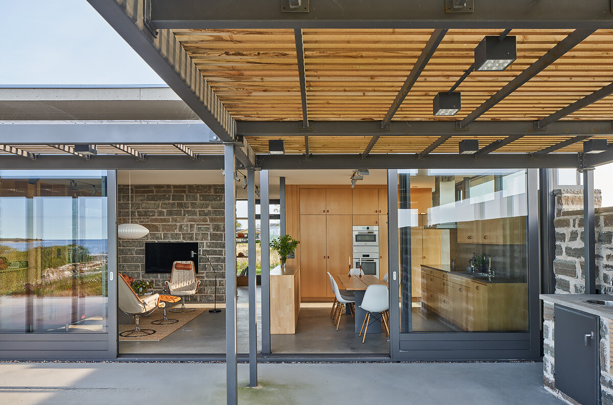 A coastal terrace with an outdoor kitchen and fireplace extends the living space, offering uninterrupted views of the sea.