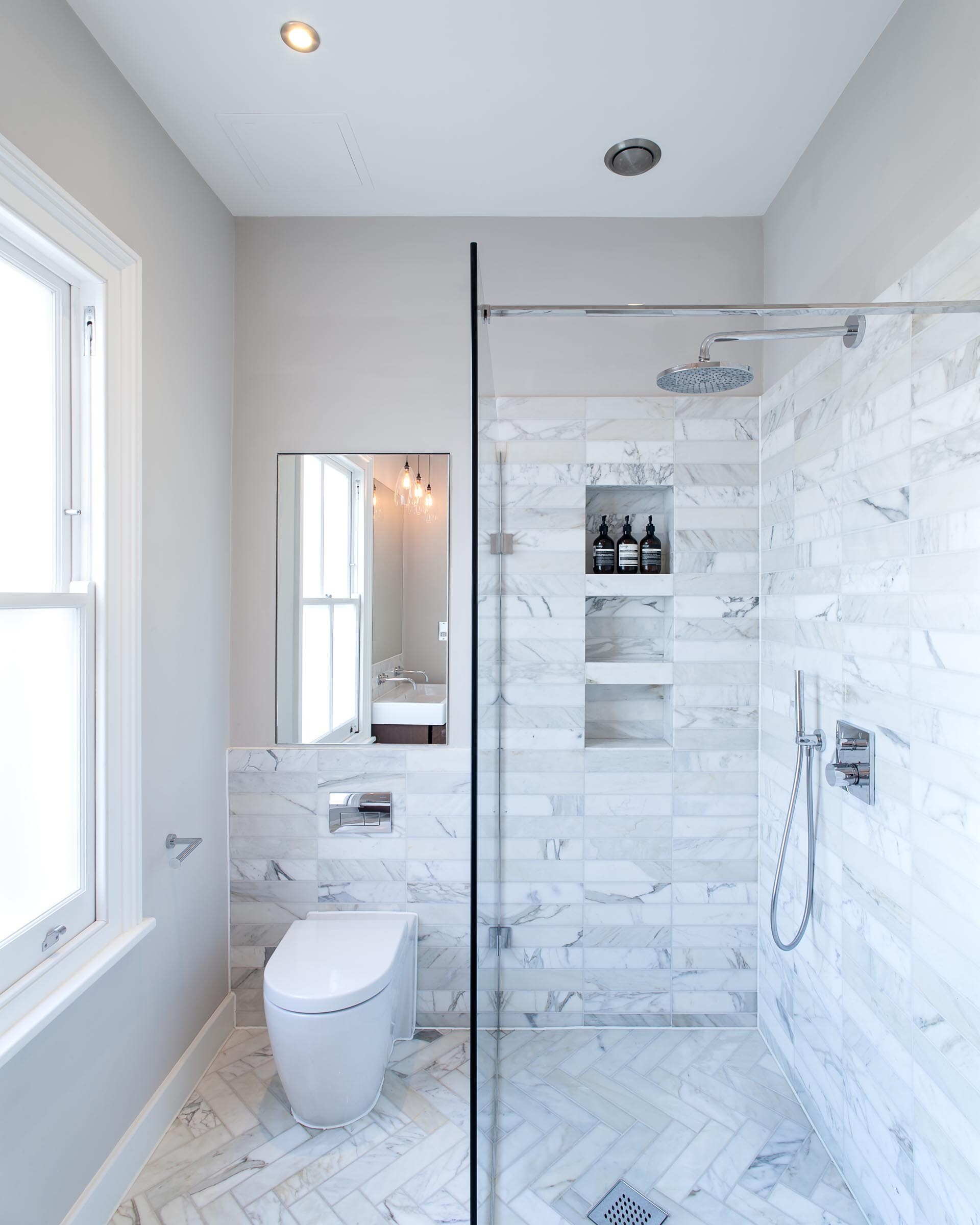 Gray stone tiles wrap the bathroom floor and walls, while three built in shower niches add practical storage.