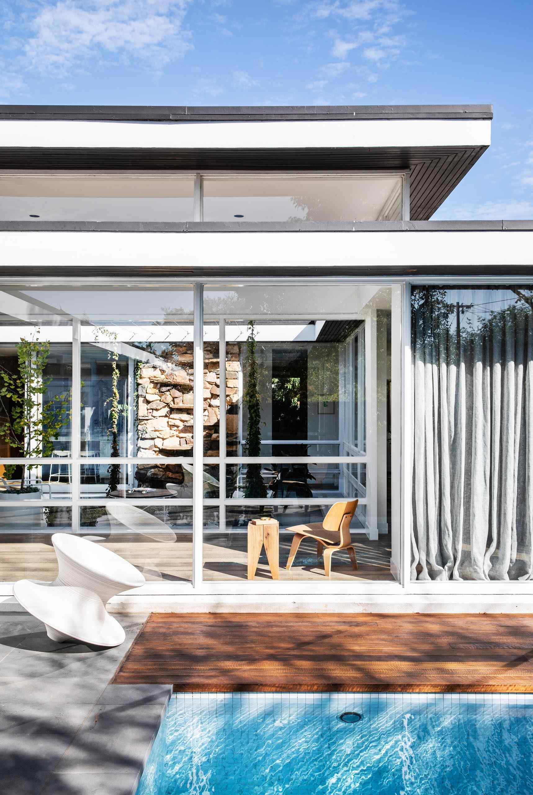 Floor-to-ceiling windows frame views of a swimming pool and wood deck just outside the house.