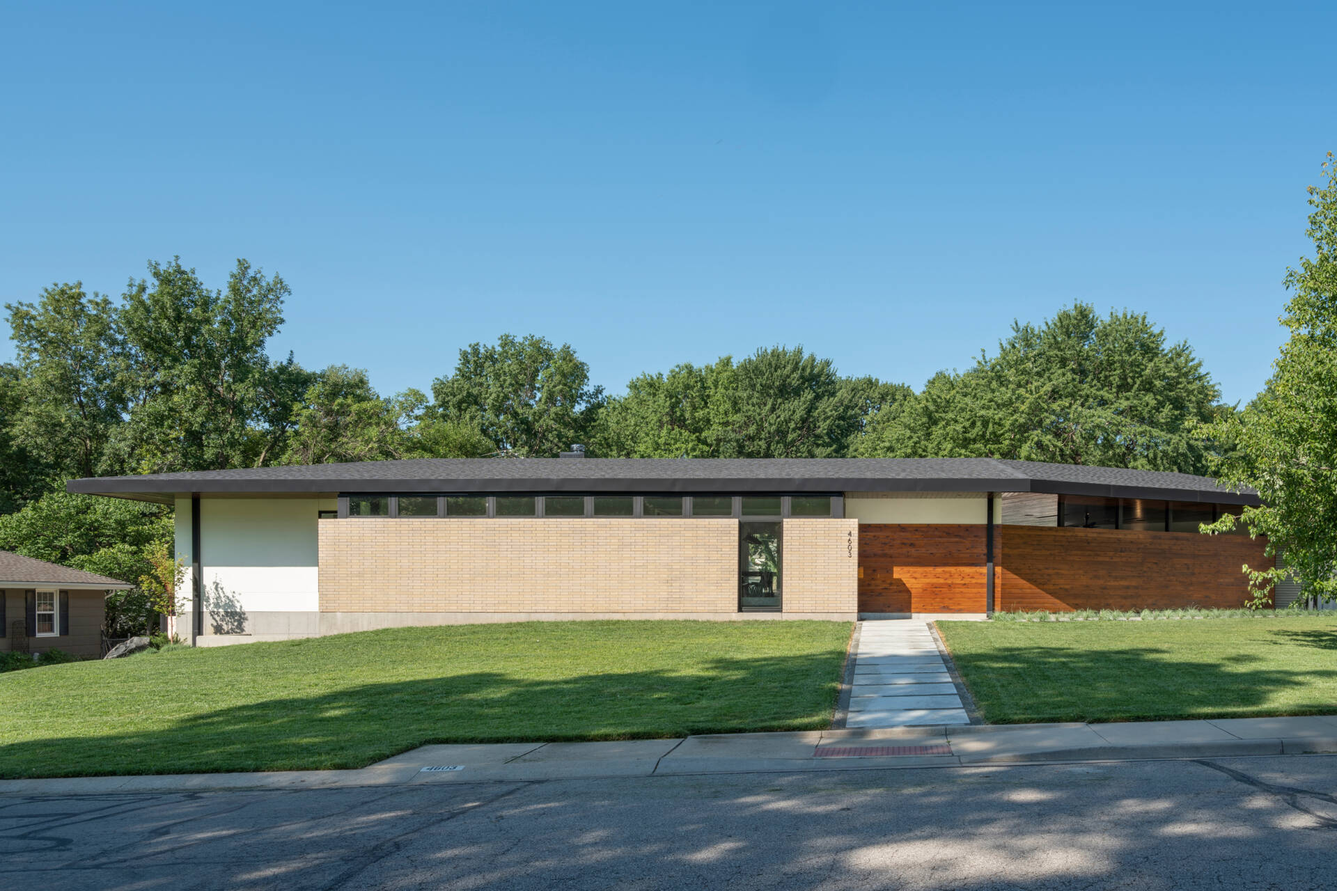 The exterior of the Homestead Residence blends light buff brick, white stucco, exposed concrete, and warm stained cedar, creating a contemporary Mid-Century Modern inspired home with a calm and balanced presence.