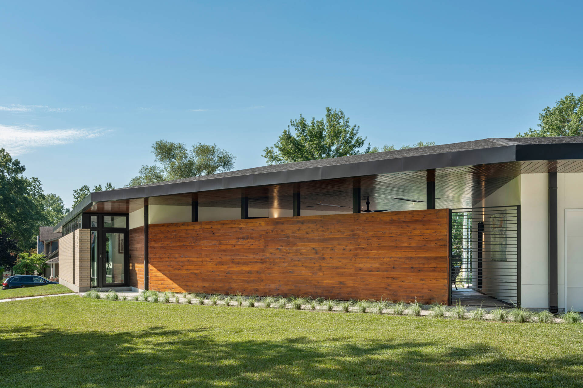 The exterior of the Homestead Residence blends light buff brick, white stucco, exposed concrete, and warm stained cedar, creating a contemporary Mid-Century Modern inspired home with a calm and balanced presence.