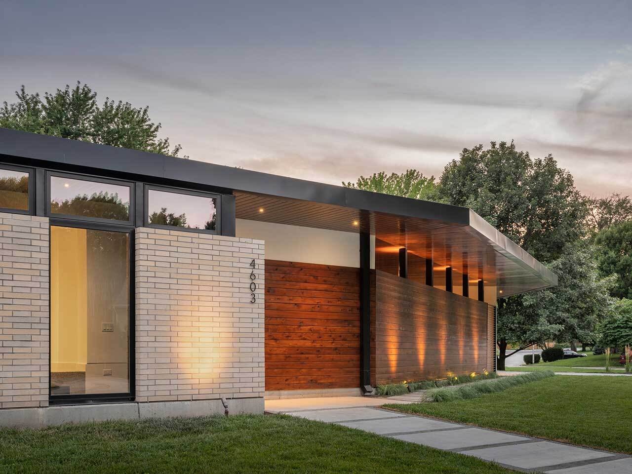 The exterior of the Homestead Residence blends light buff brick, white stucco, exposed concrete, and warm stained cedar, creating a contemporary Mid-Century Modern inspired home with a calm and balanced presence.