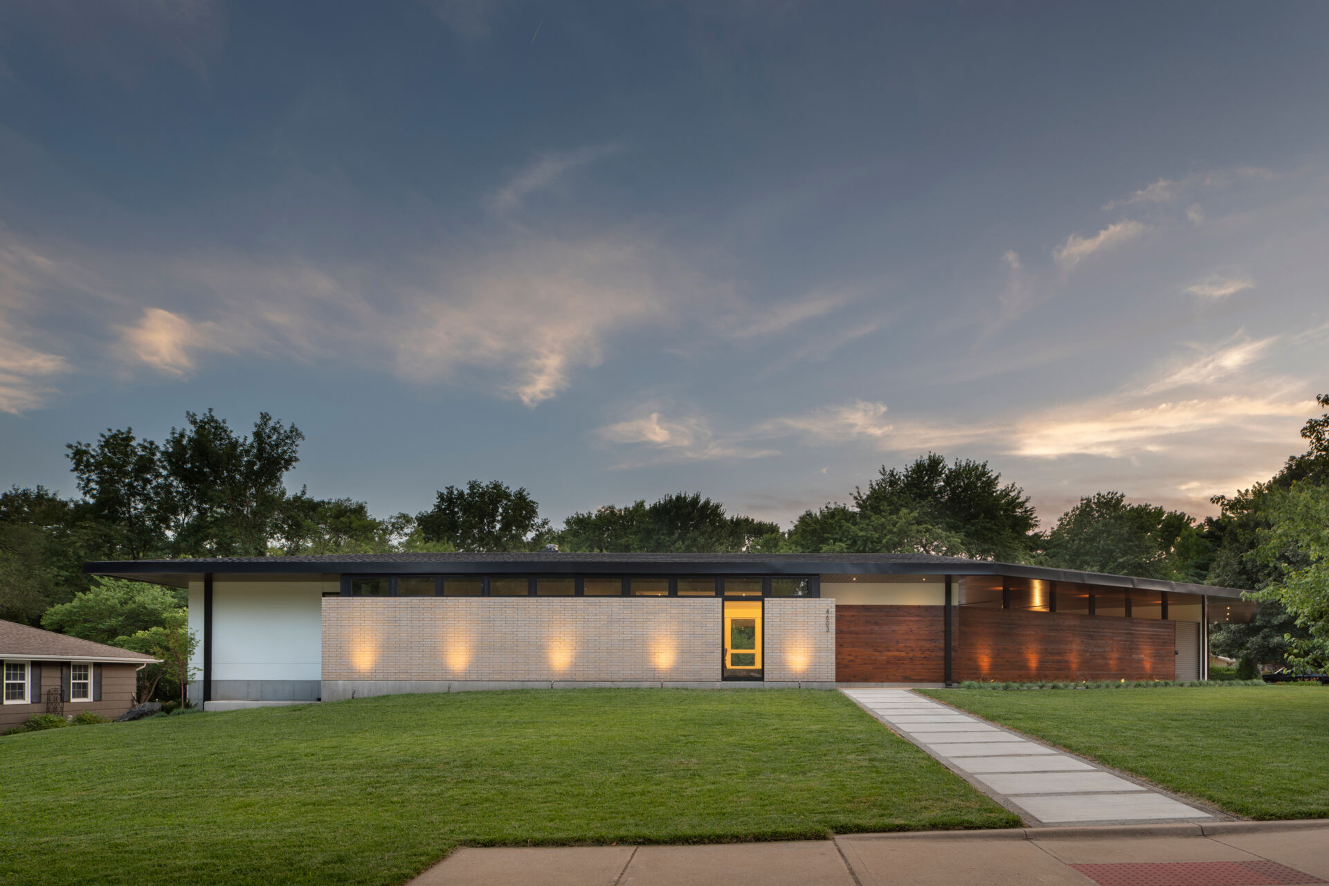 The exterior of the Homestead Residence blends light buff brick, white stucco, exposed concrete, and warm stained cedar, creating a contemporary Mid-Century Modern inspired home with a calm and balanced presence.