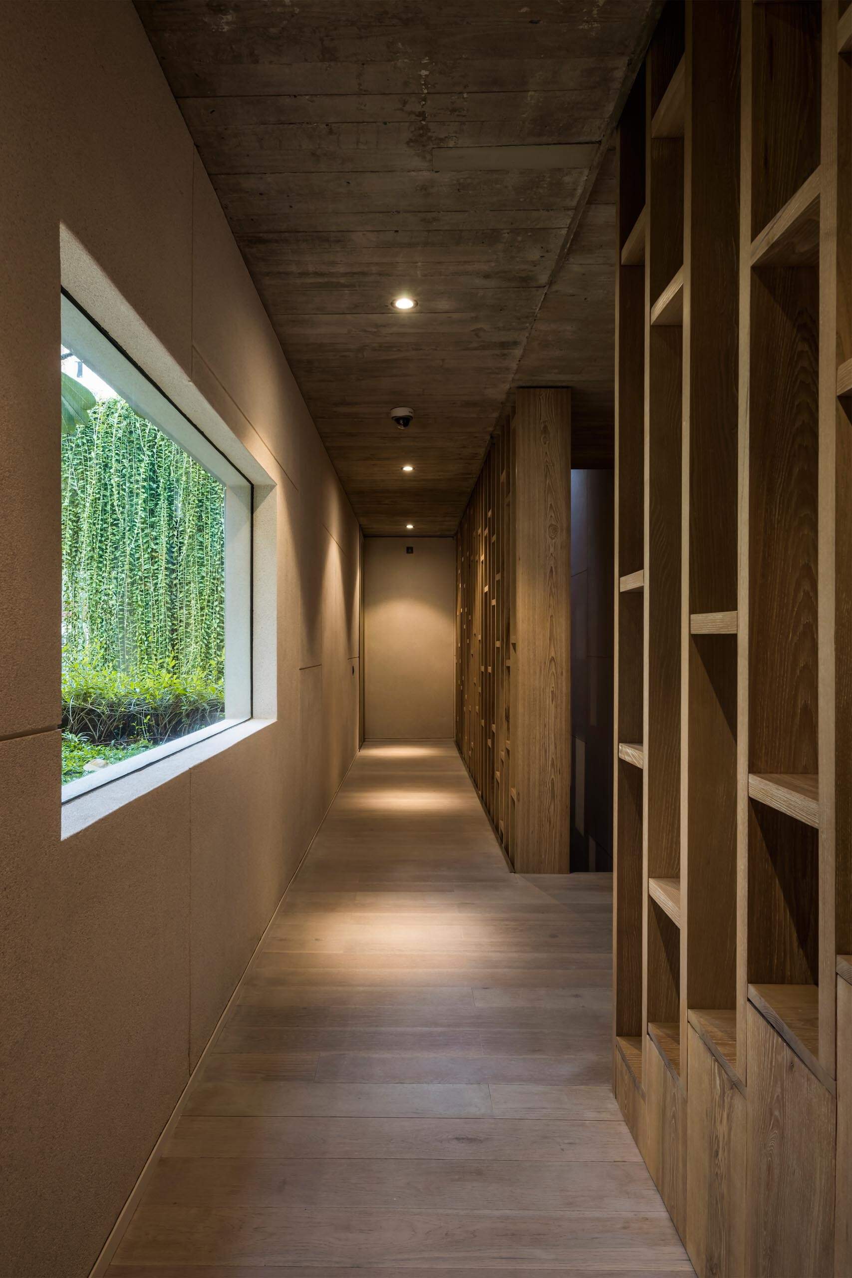 Las paredes de hormigón en bruto, las cálidas escaleras de madera y la luz filtrada crean un ambiente interior relajante, con plantas y materiales naturales que suavizan la arquitectura.