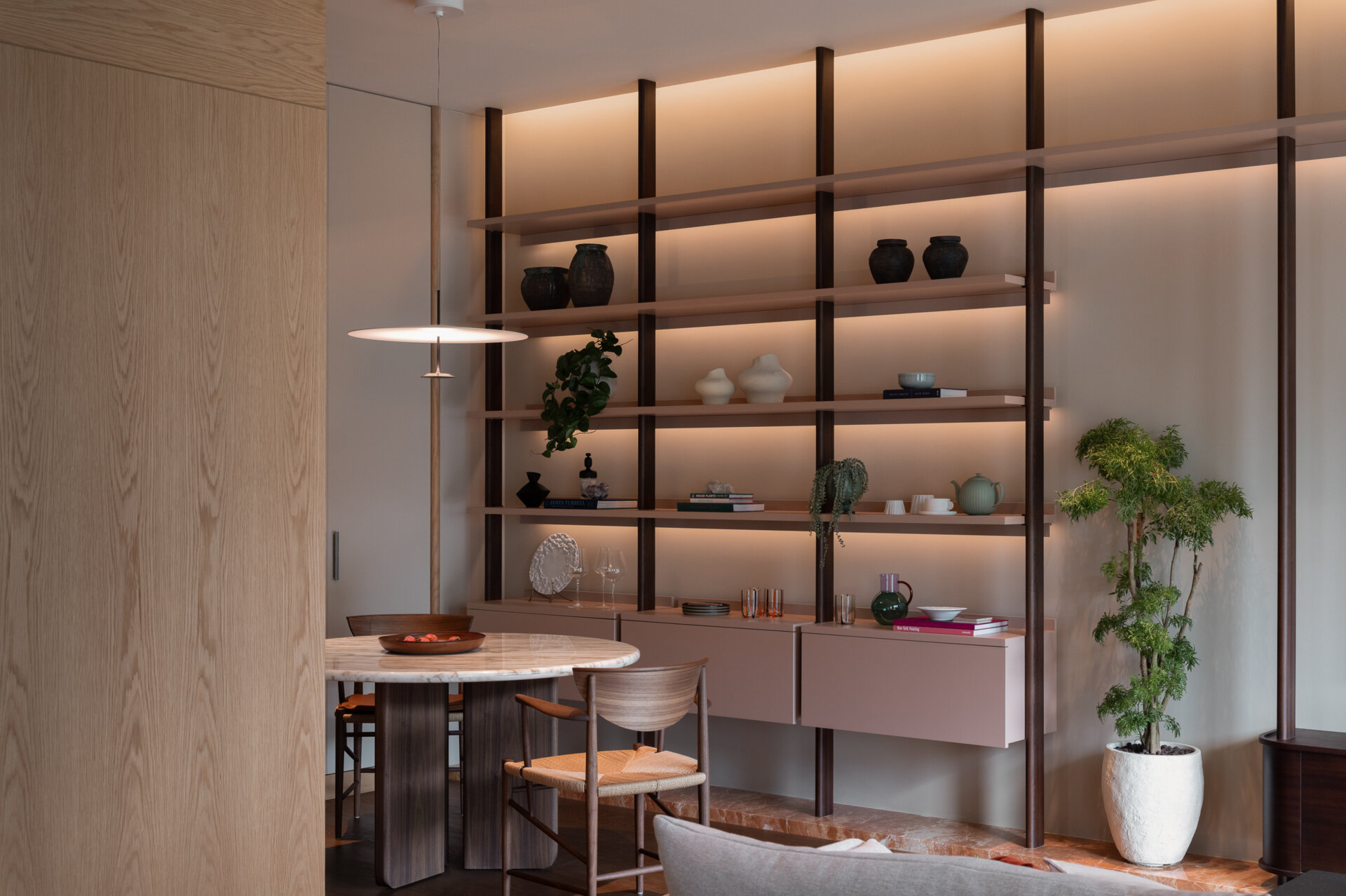 In the dining area, a custom bookshelf and soft lighting create a warm, layered atmosphere that connects seamlessly with the living space.
