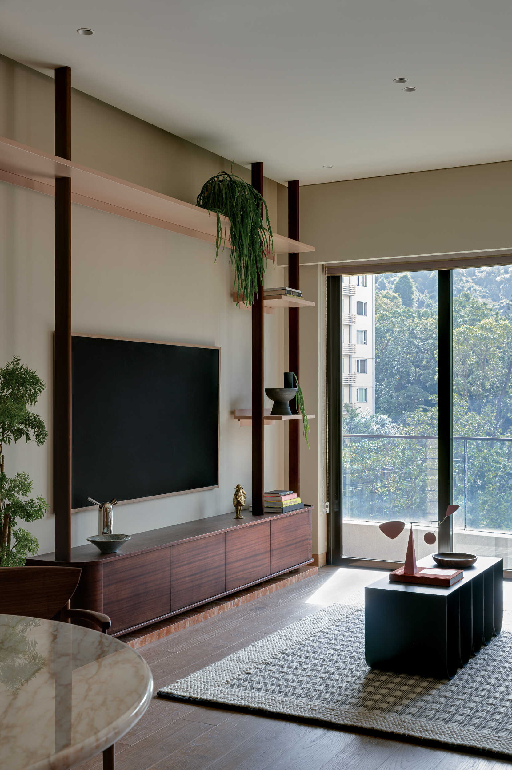 By opening up an extra bedroom, the living room now expands into a light-filled zone that forms the heart of the home.

Daylight moves laterally across the space, reaching deeper into areas that were once dim. A sapele-veneer TV cabinet sits against the wall, while a sliding door opens to a balcony.