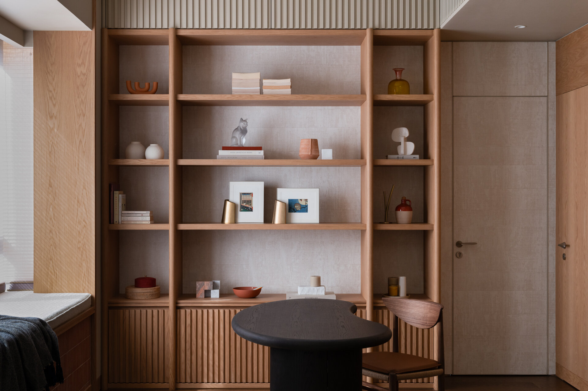 In the study area, a curved oak desk and open shelving create a quiet workspace that remains visually connected to the rest of the home.