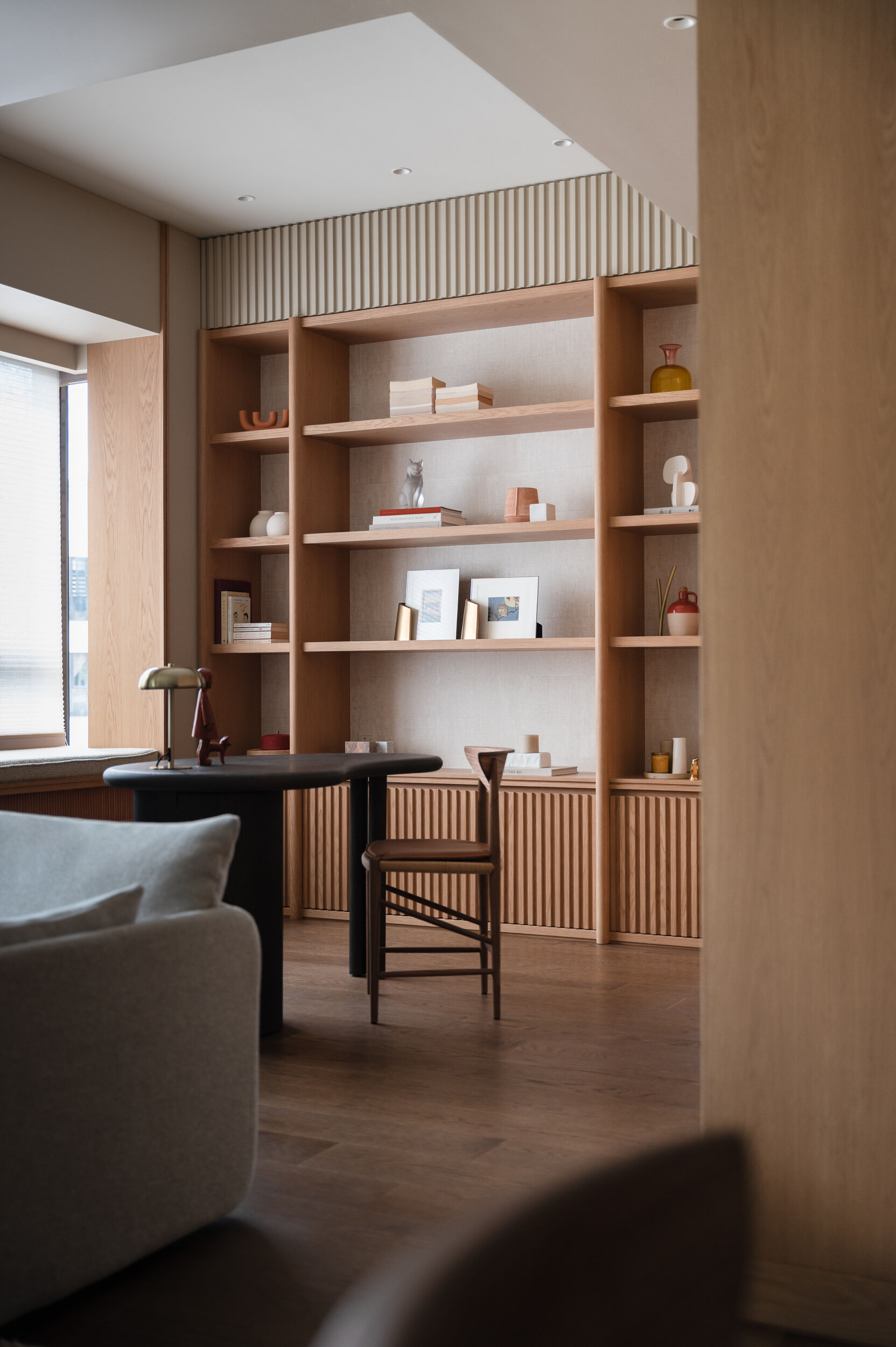 In the study area, a curved oak desk and open shelving create a quiet workspace that remains visually connected to the rest of the home.