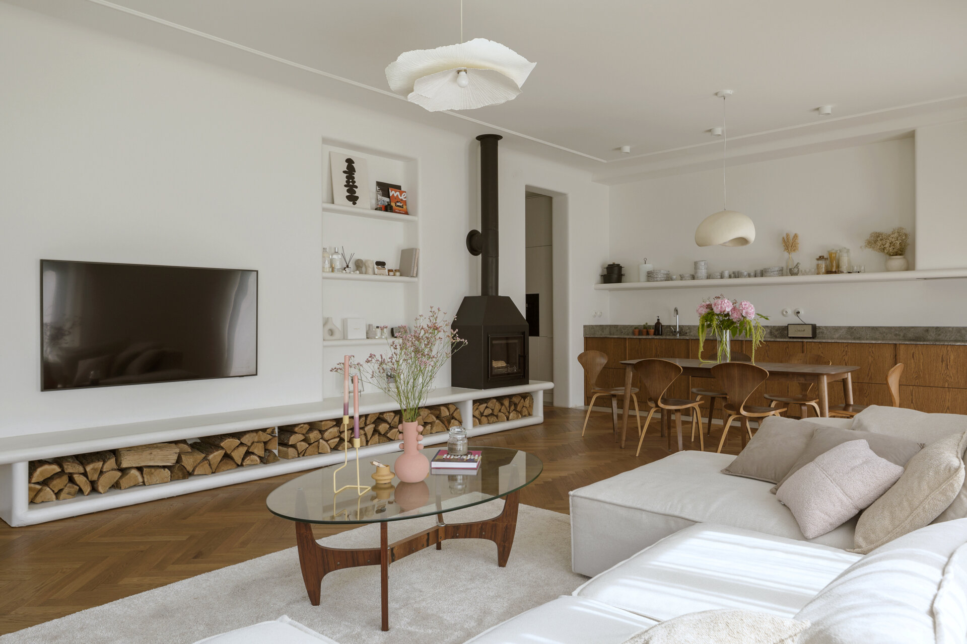 A modern living room with a long, multi-functional unit that integrates the firewood storage while doubling as seating. A built-in shelving niche and fireplace finish the living room space.